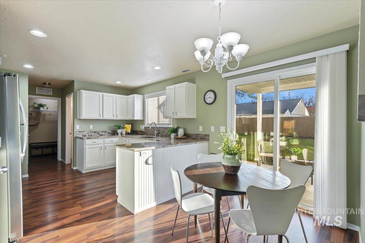 Kitchen with white cabinetry, light stone countertops, dark wood-style floors, freestanding refrigerator, and a peninsula