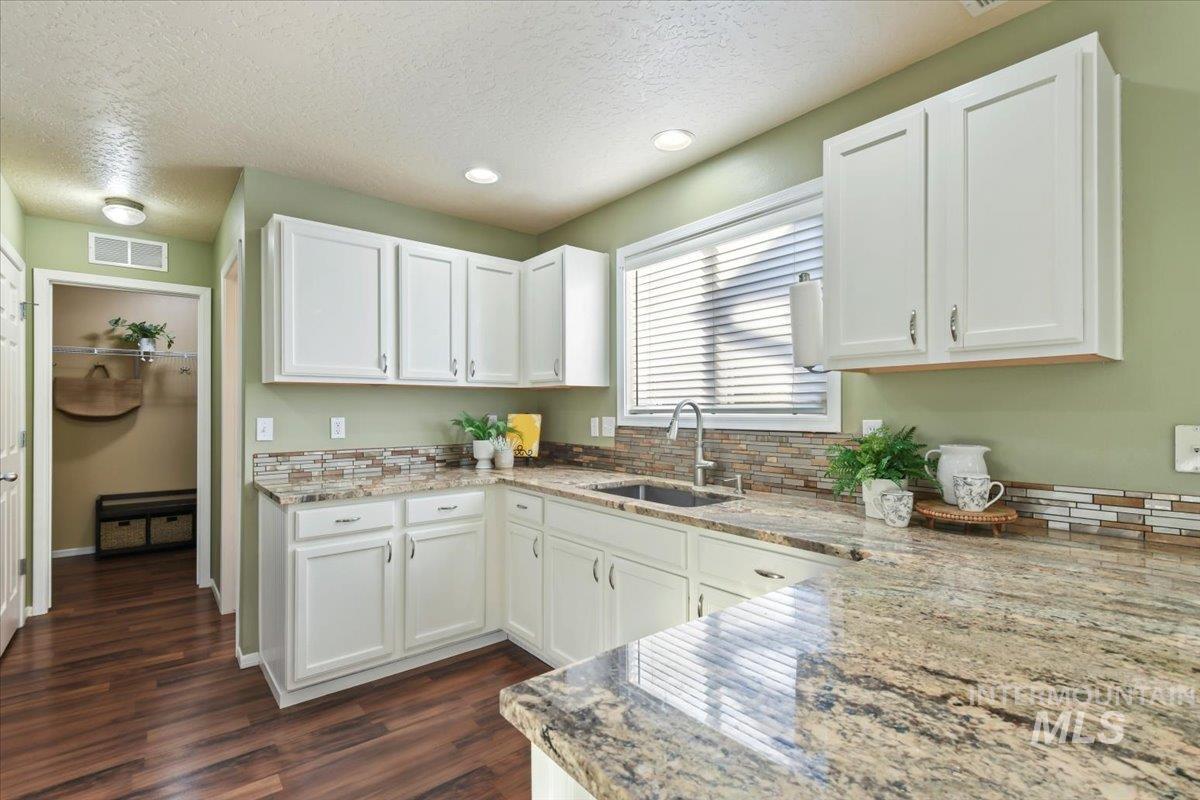 Kitchen with white cabinets, light stone counters, a textured ceiling, dark wood-type flooring, and recessed lighting