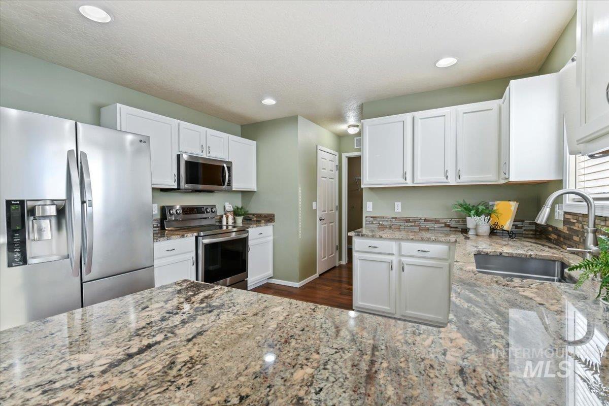 Kitchen with appliances with stainless steel finishes, white cabinets, light stone counters, recessed lighting, and dark wood finished floors