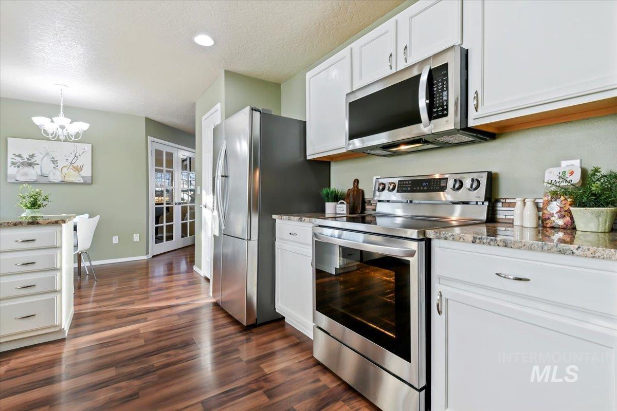 Kitchen with stainless steel appliances, a textured ceiling, white cabinets, light stone countertops, and dark wood-style floors