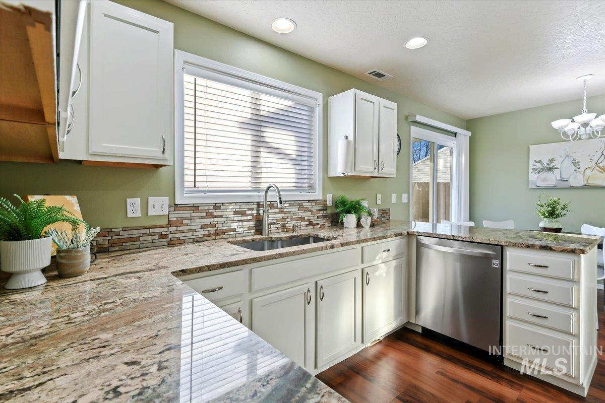 Kitchen with white cabinets, light stone countertops, stainless steel dishwasher, a peninsula, and dark wood-type flooring