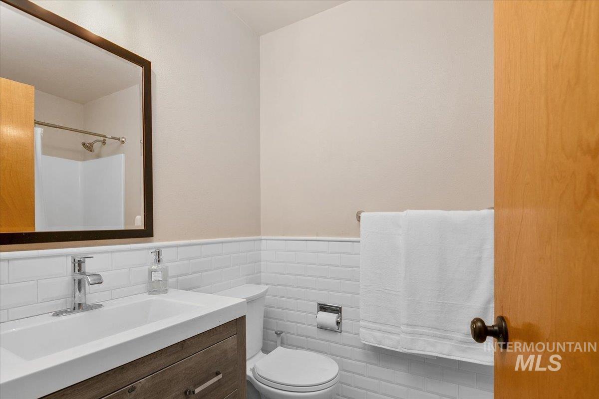 Bathroom with vanity, a shower, a wainscoted wall, and tile walls