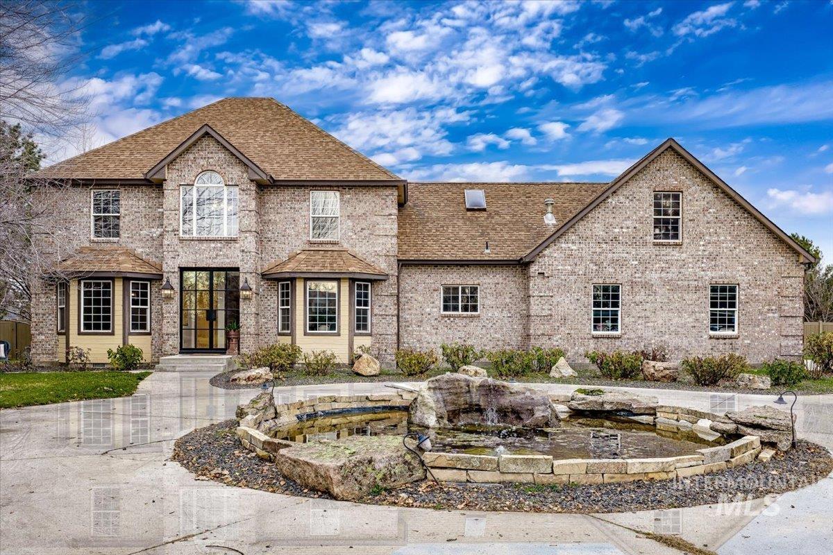 View of front facade featuring brick siding, roof with shingles, and a garden pond