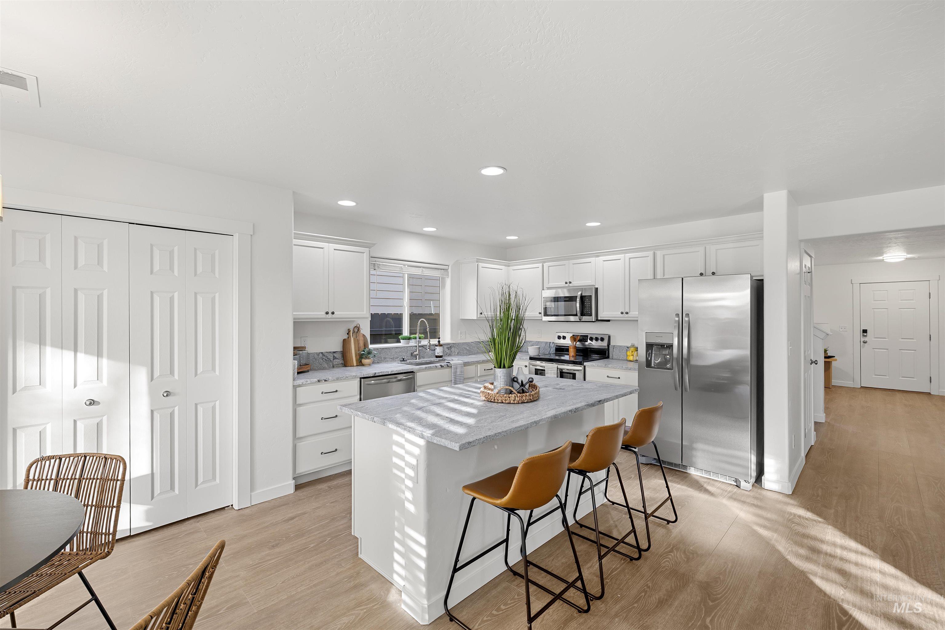 Kitchen featuring a breakfast bar, stainless steel appliances, light stone counters, white cabinetry, and recessed lighting