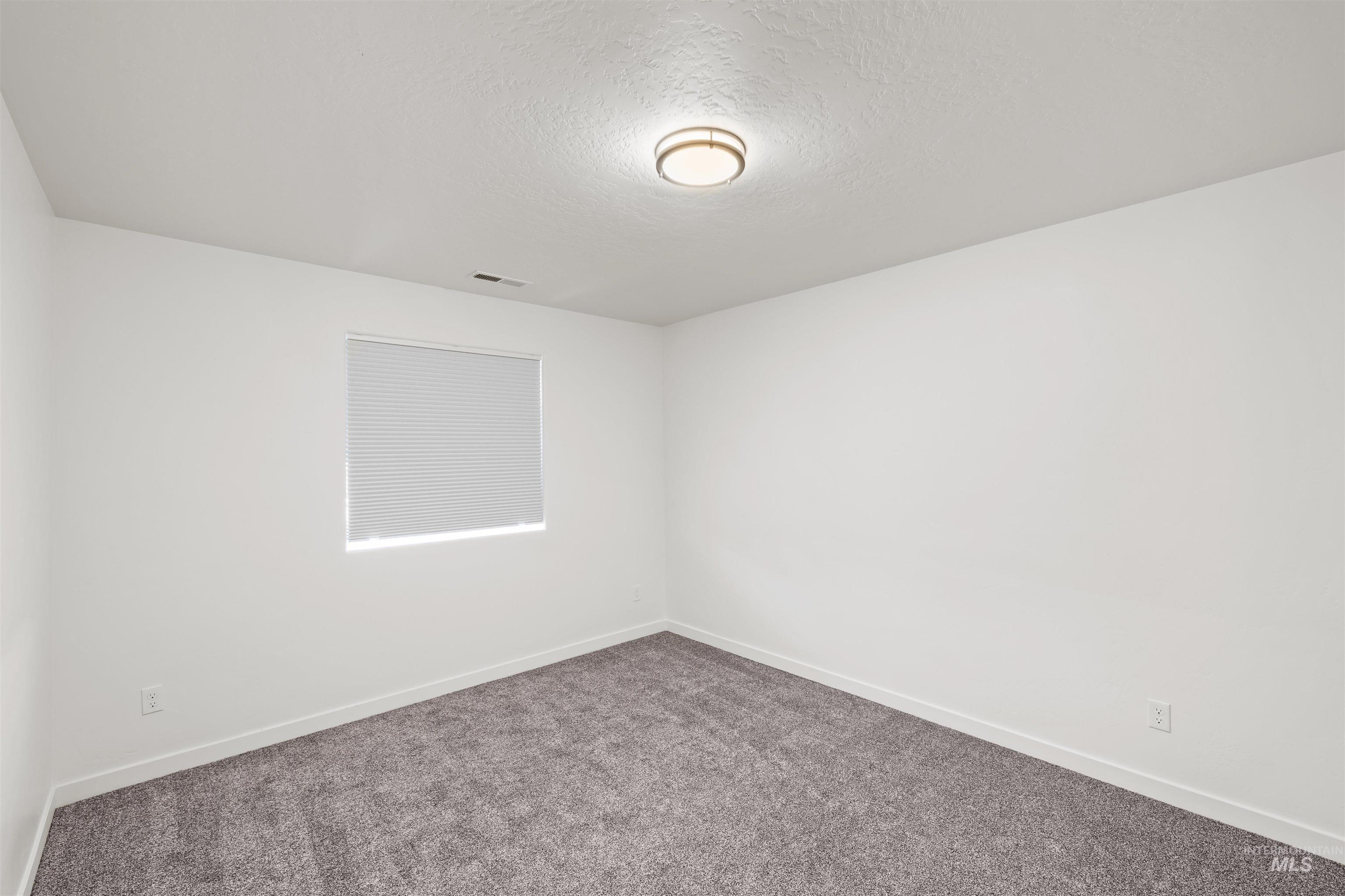 Carpeted empty room featuring a textured ceiling and baseboards