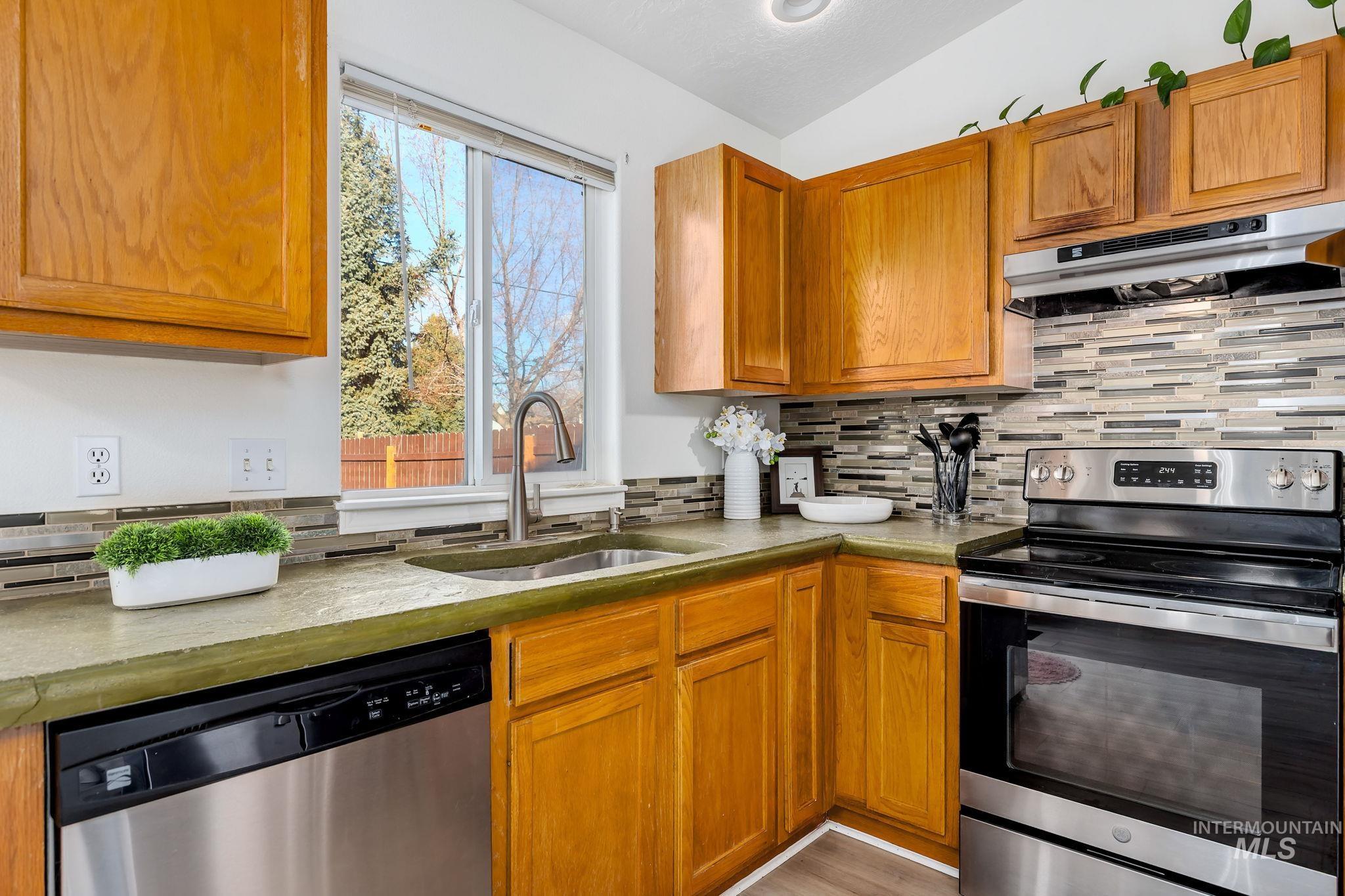Kitchen featuring appliances with stainless steel finishes, under cabinet range hood, lofted ceiling, brown cabinets, and light countertops