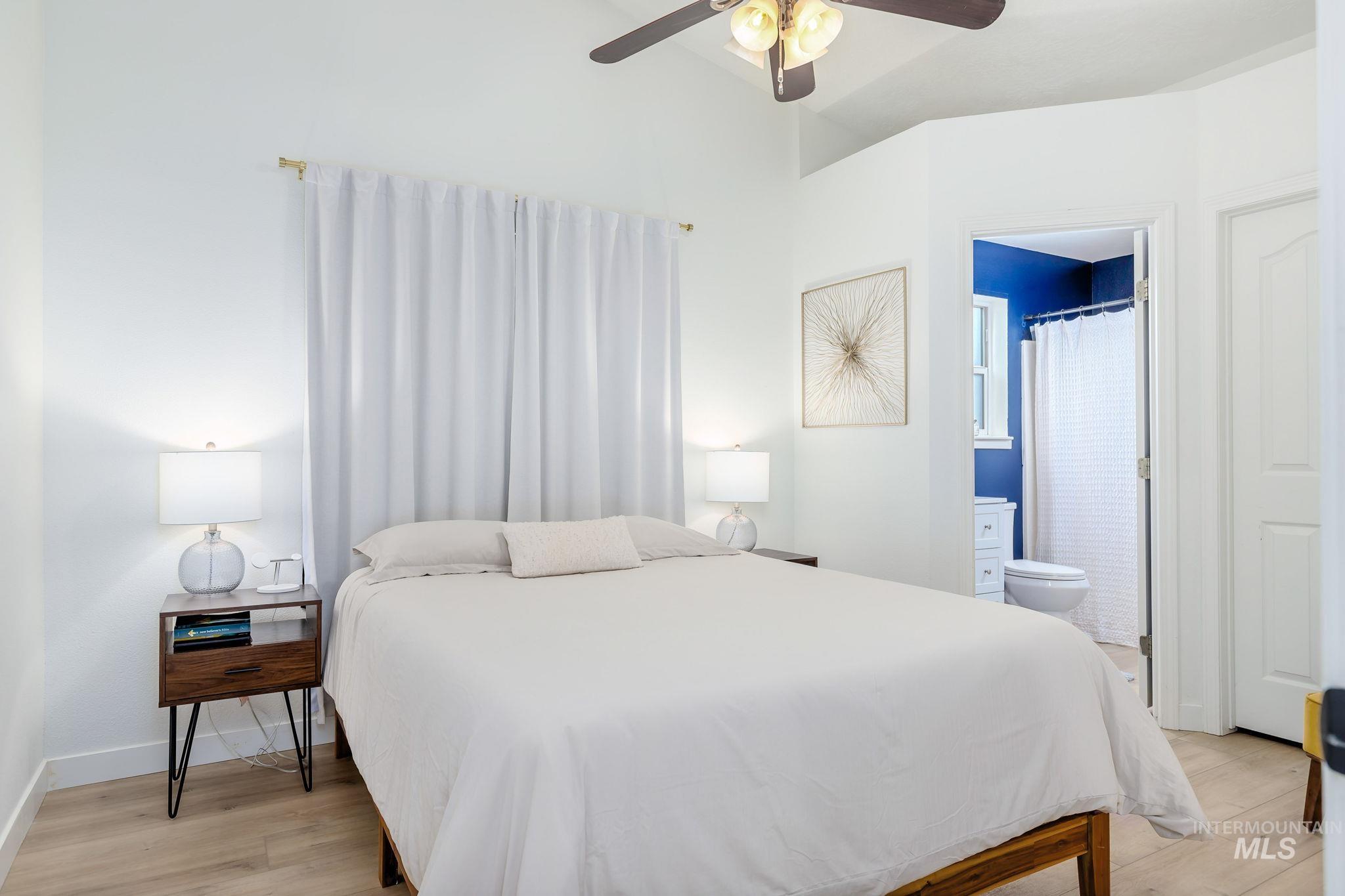 Bedroom with light wood-style floors, ceiling fan, and ensuite bath