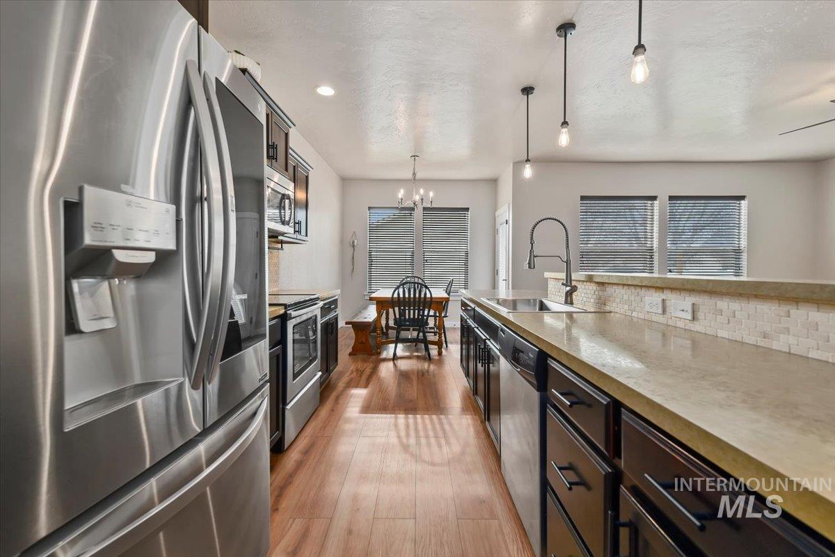 Kitchen with appliances with stainless steel finishes, decorative light fixtures, a chandelier, dark wood-style flooring, and dark brown cabinets