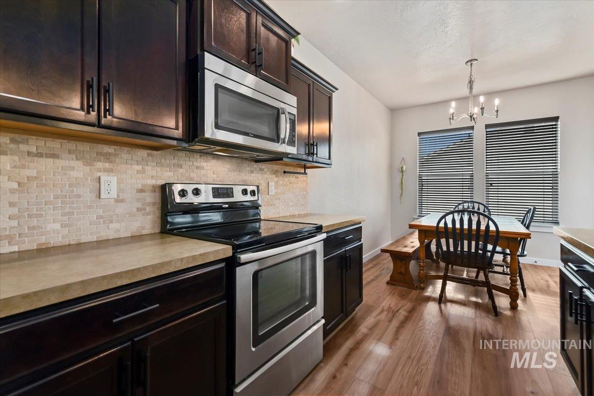 Kitchen featuring stainless steel appliances, decorative light fixtures, light countertops, a chandelier, and tasteful backsplash