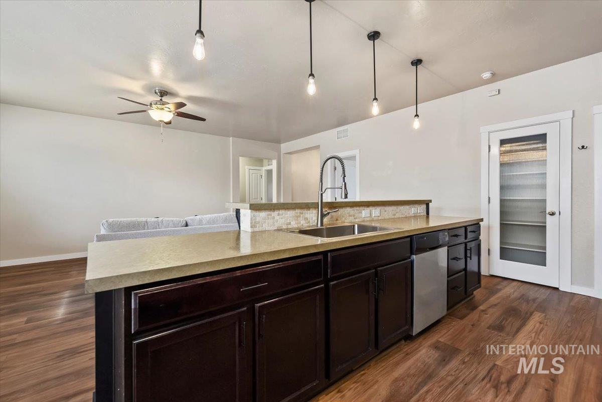 Kitchen with light countertops, hanging light fixtures, a center island with sink, dark brown cabinets, and dishwasher