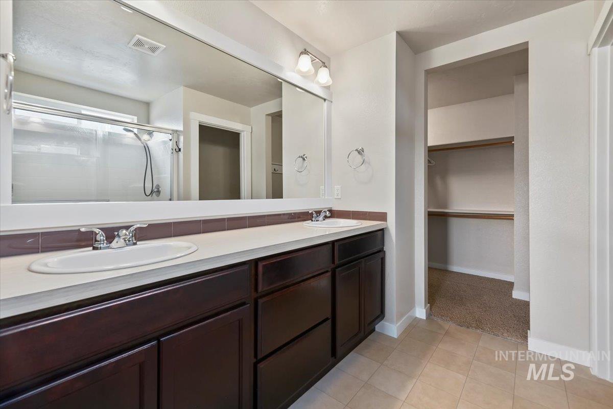 Bathroom with double vanity, a stall shower, a spacious closet, and light tile patterned floors