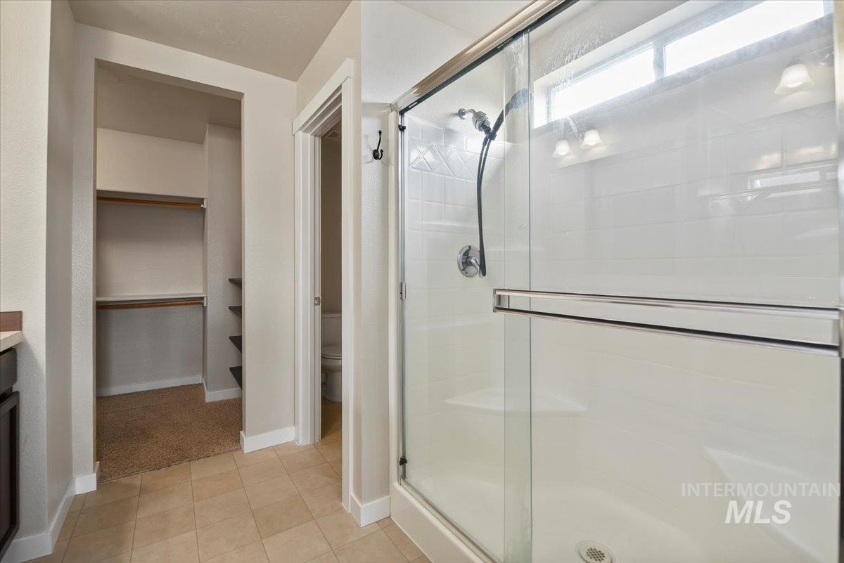 Full bath with a walk in closet, vanity, a stall shower, and light tile patterned floors