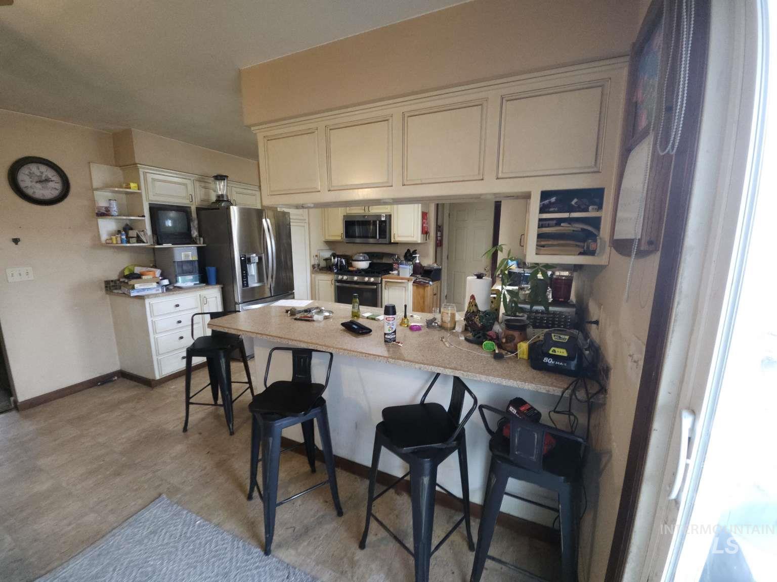Kitchen featuring a peninsula, a kitchen bar, open shelves, light countertops, and appliances with stainless steel finishes