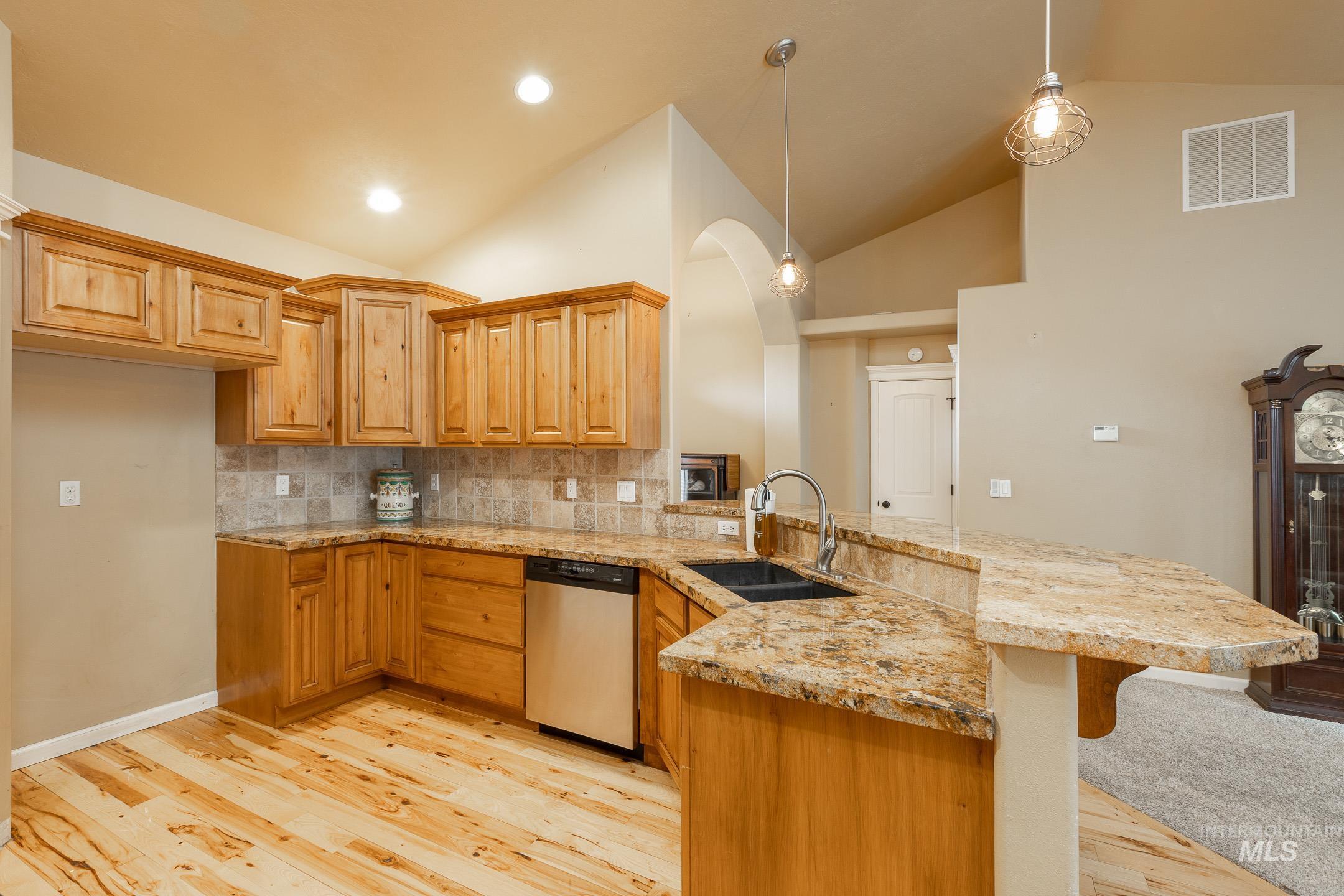 Kitchen featuring a peninsula, hanging light fixtures, stainless steel dishwasher, decorative backsplash, and brown cabinets