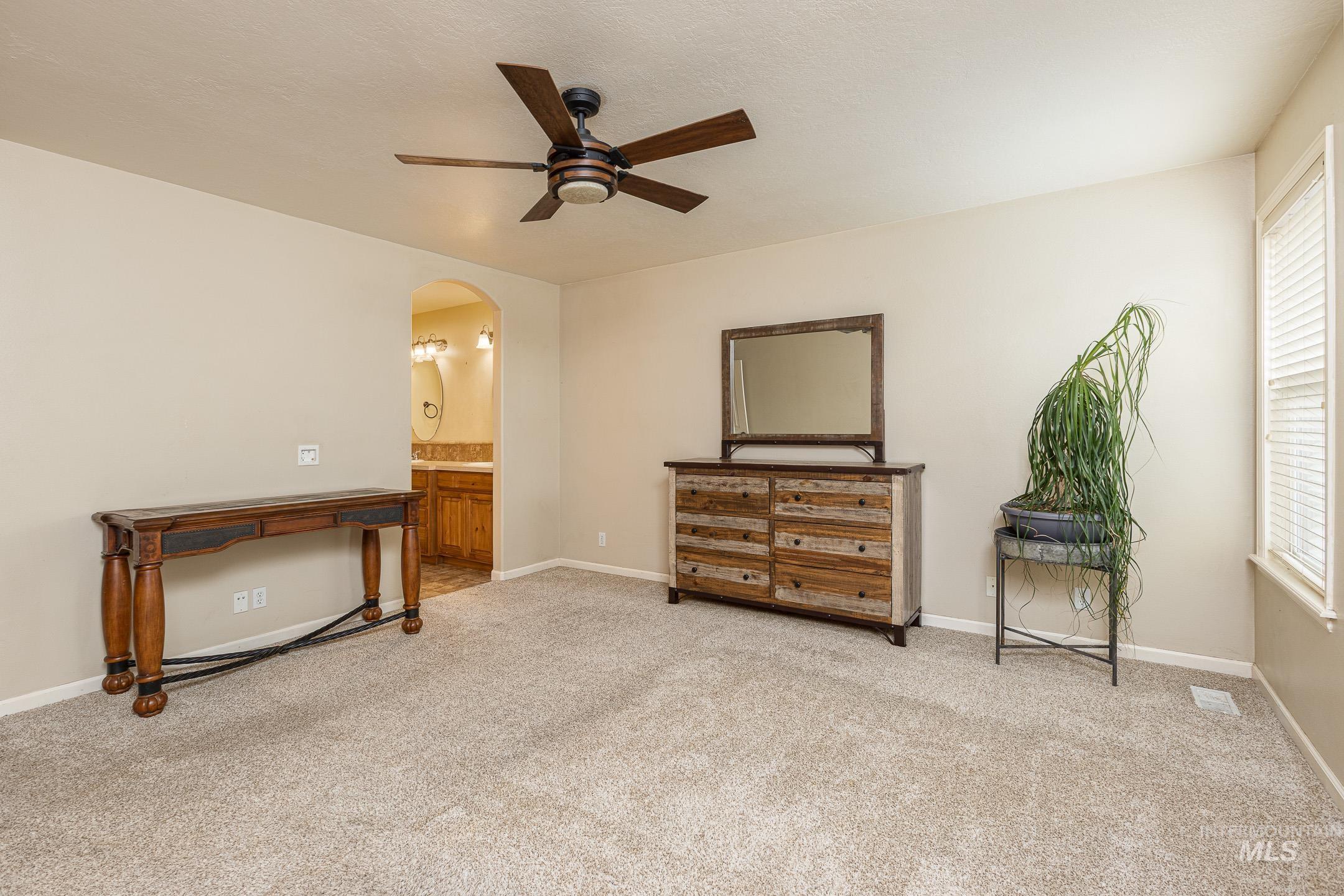 Bedroom with light carpet, a ceiling fan, arched walkways, and ensuite bathroom