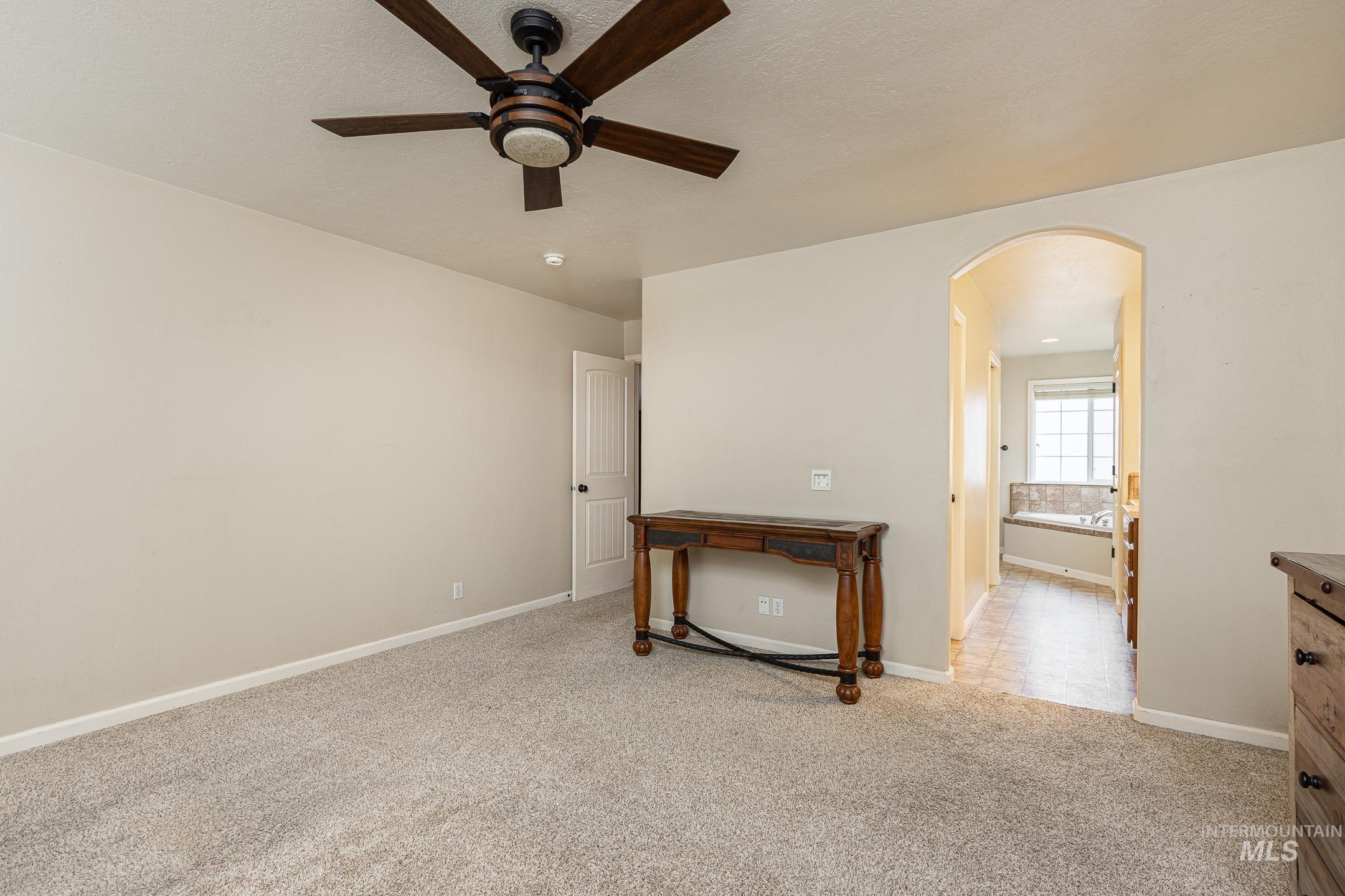 Unfurnished room featuring light carpet, arched walkways, and a ceiling fan