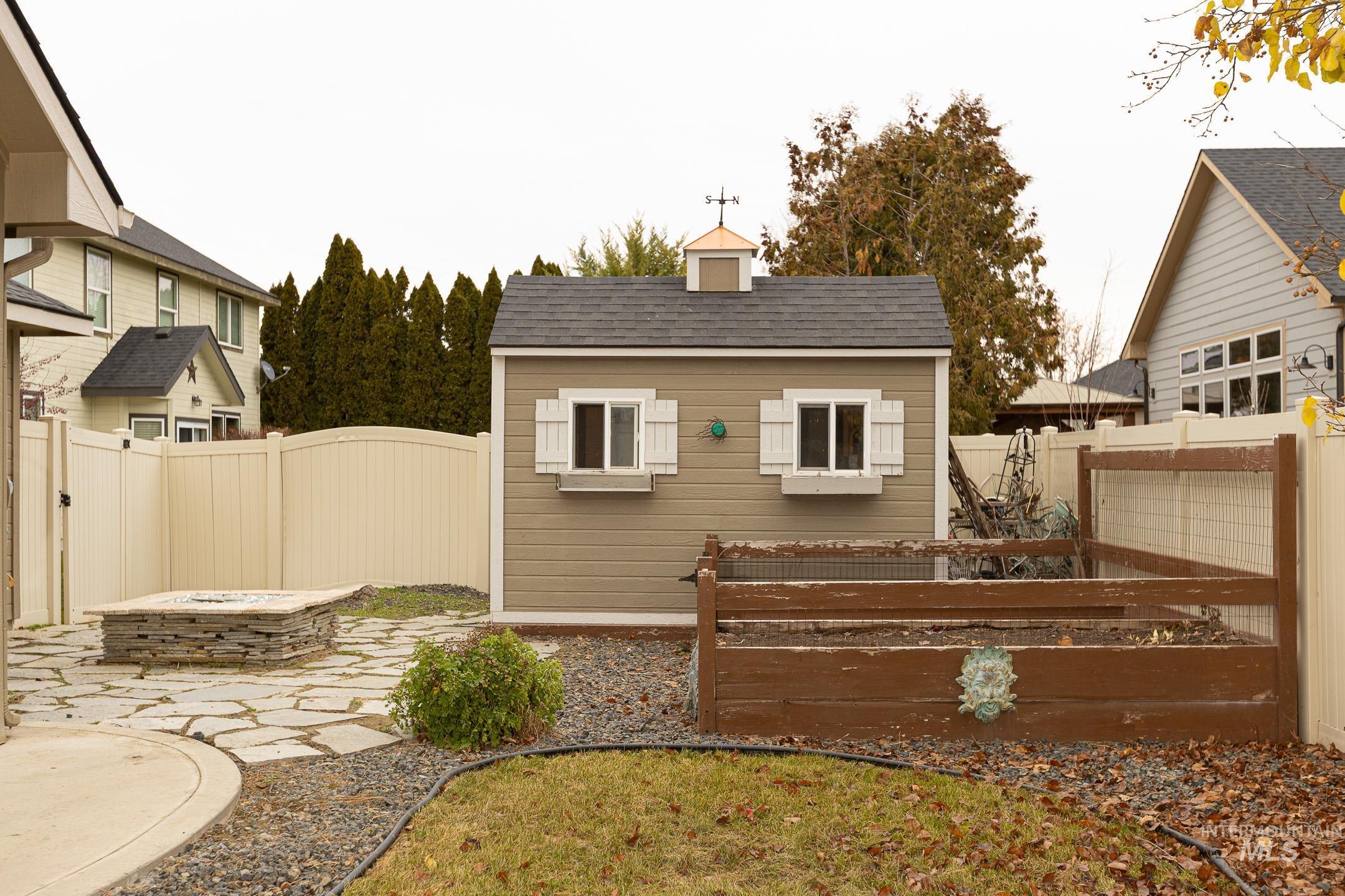 Back of property with a fire pit, a garden, a fenced backyard, a patio, and an outdoor structure