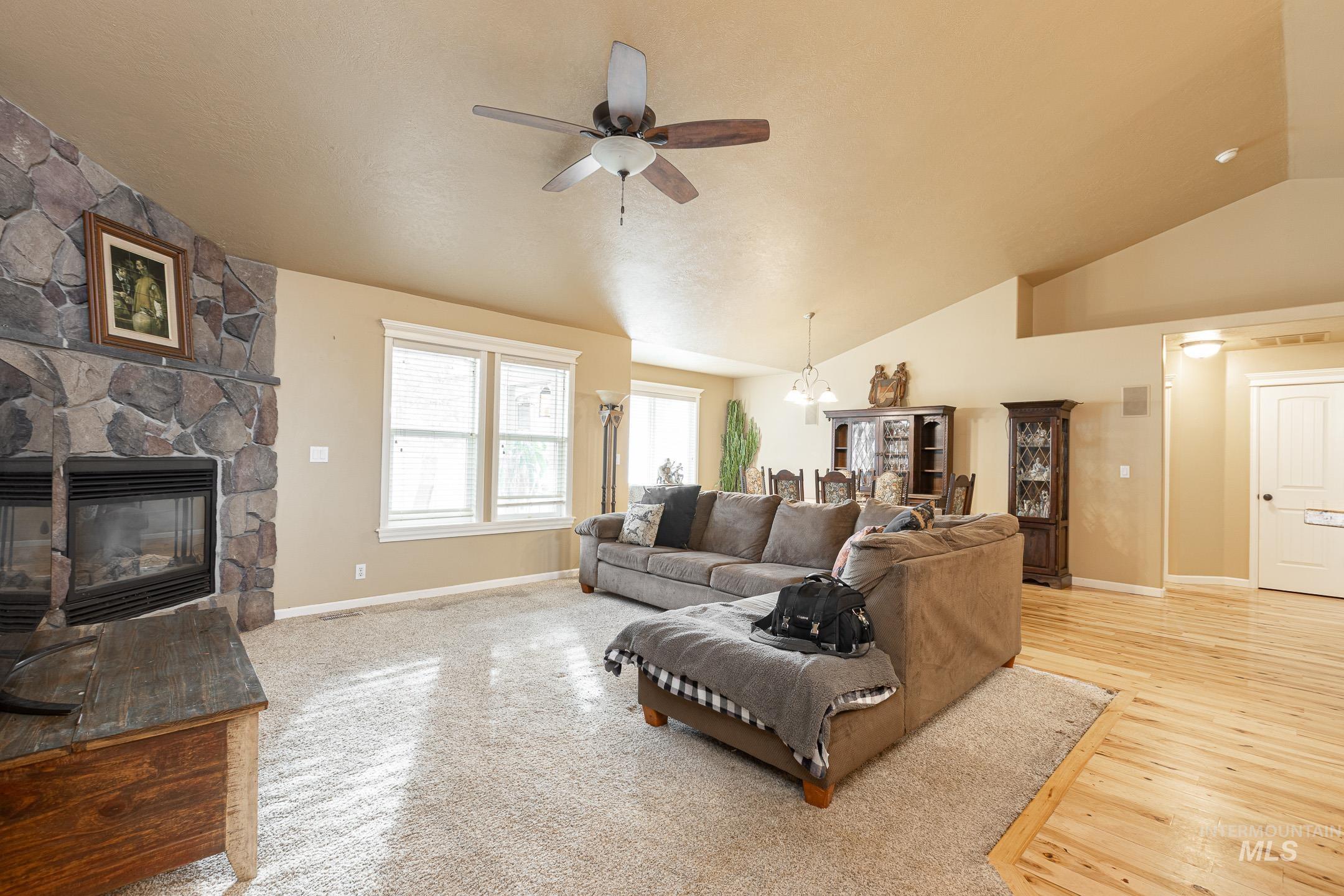 Living area featuring vaulted ceiling, a fireplace, ceiling fan, a chandelier, and light wood-style floors
