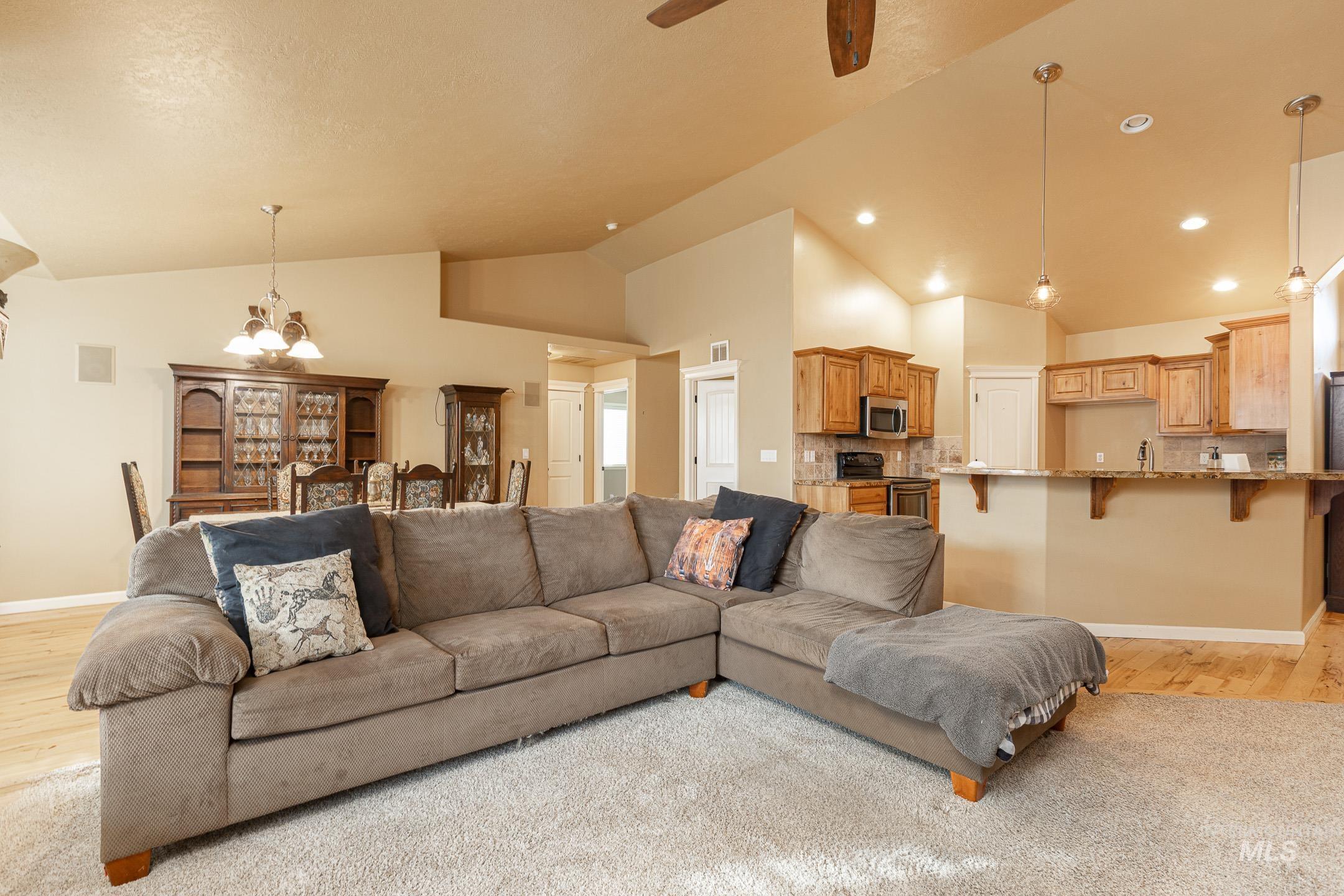 Living room featuring a chandelier, light wood-style flooring, high vaulted ceiling, and a ceiling fan