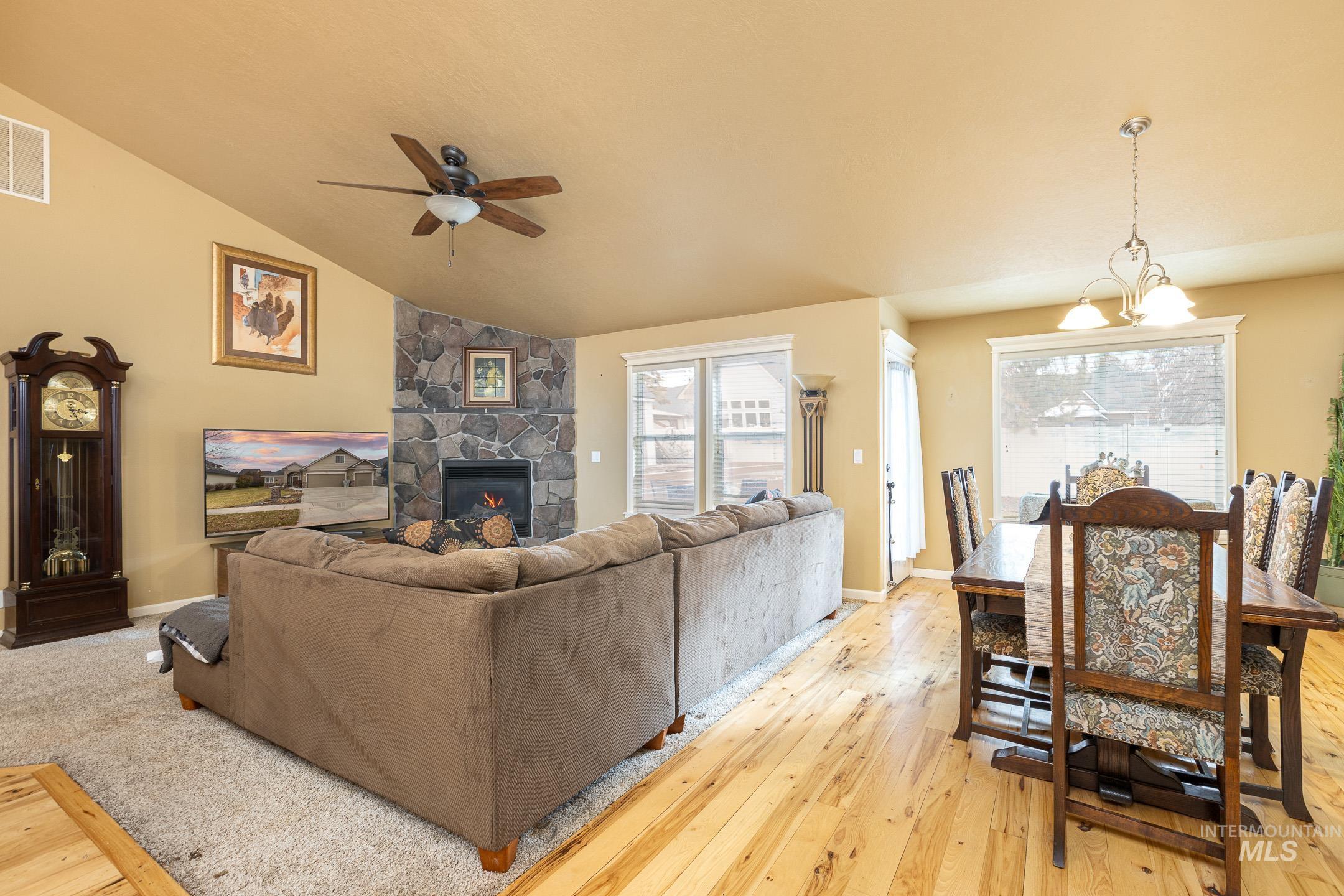 Living room with a fireplace, a chandelier, light wood finished floors, lofted ceiling, and ceiling fan