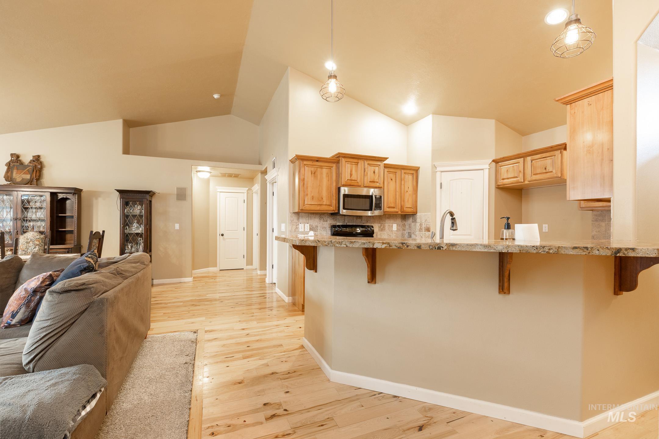 Kitchen with a kitchen bar, open floor plan, a peninsula, light stone counters, and stainless steel microwave