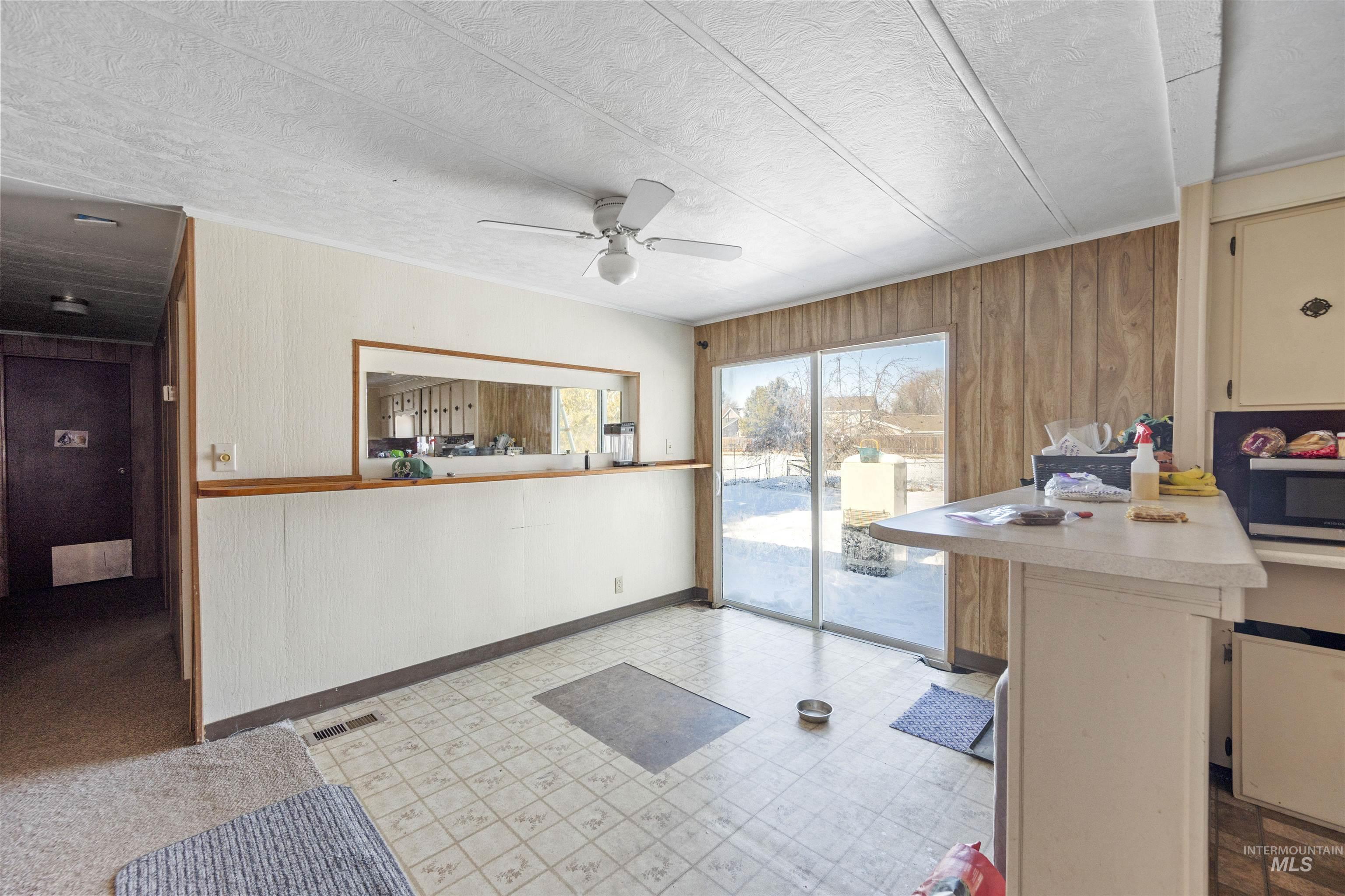 Kitchen with light flooring, wood walls, light countertops, a ceiling fan, and stainless steel microwave