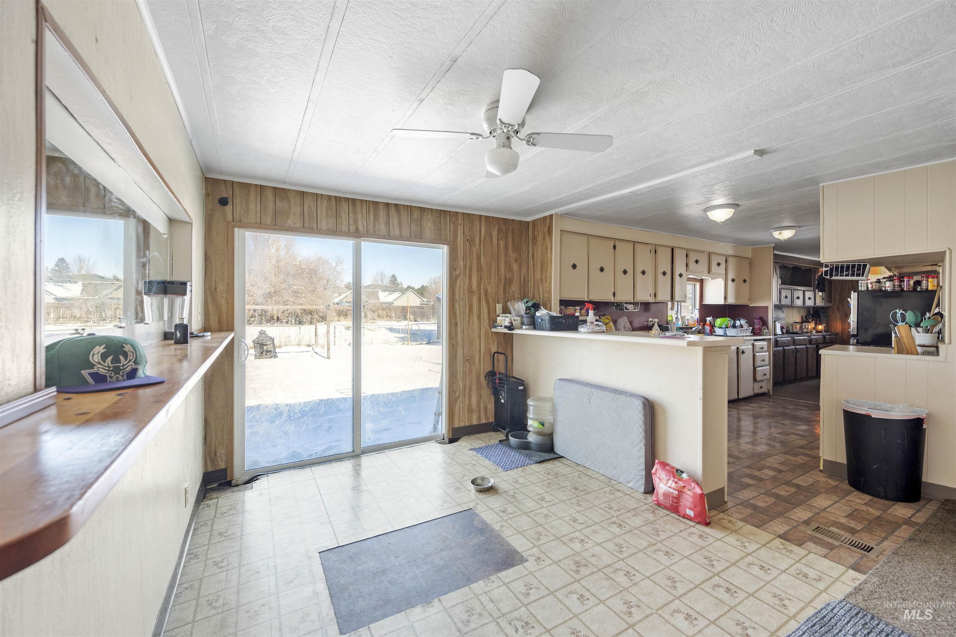 Kitchen featuring wood walls, light flooring, healthy amount of natural light, a peninsula, and a ceiling fan