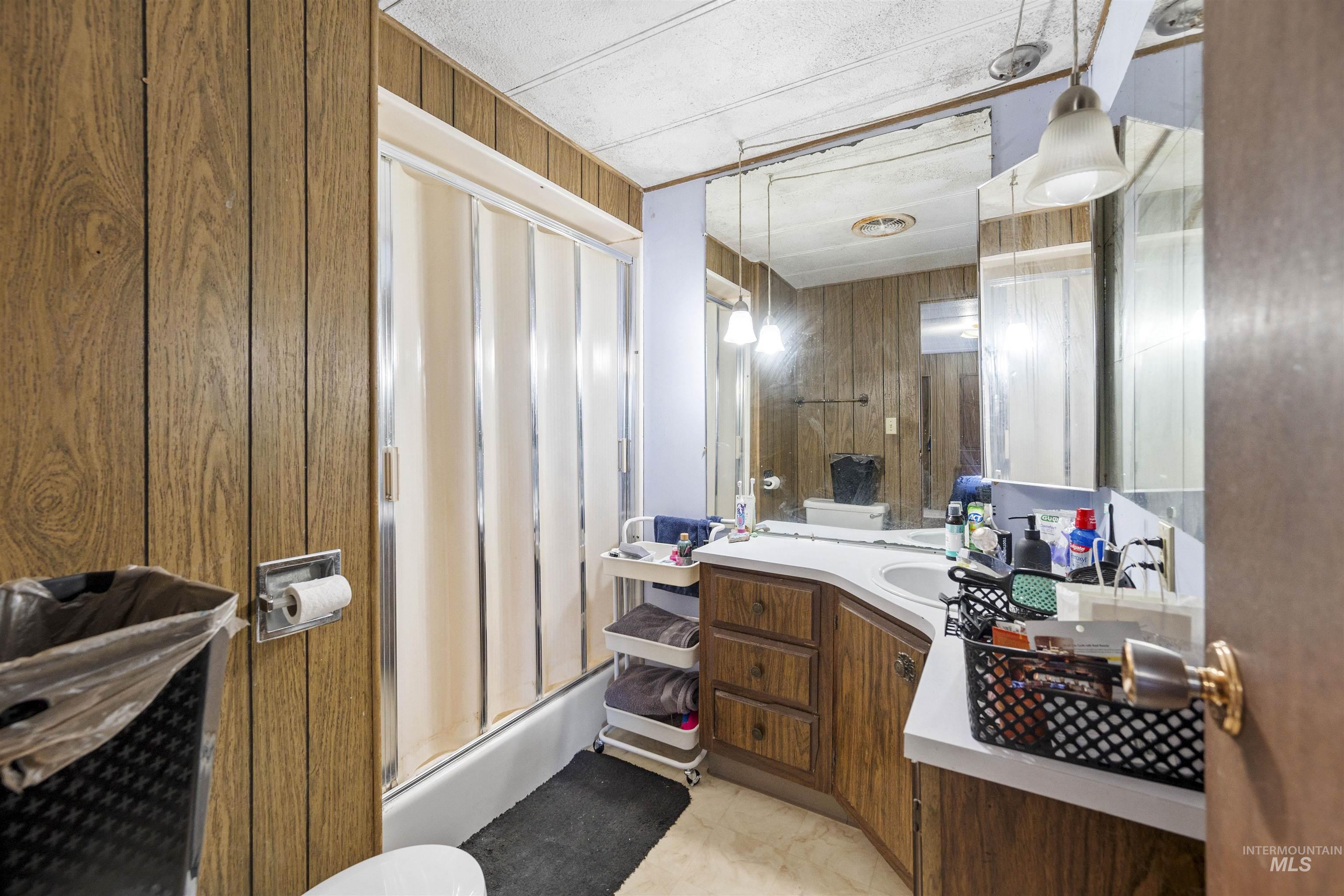 Bathroom featuring wood walls, vanity, and enclosed tub / shower combo