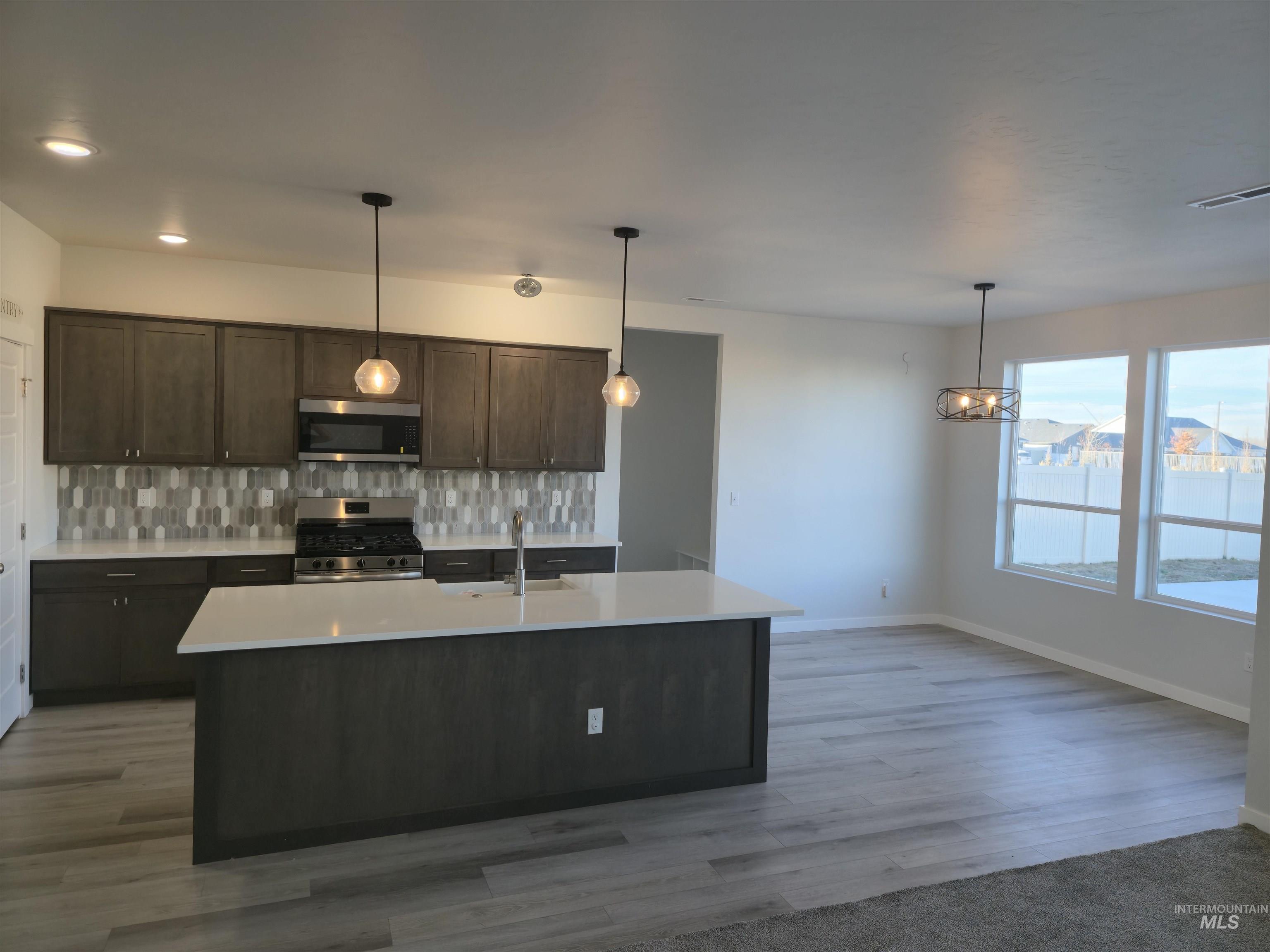 Kitchen with dark brown cabinetry, tasteful backsplash, appliances with stainless steel finishes, and pendant lighting