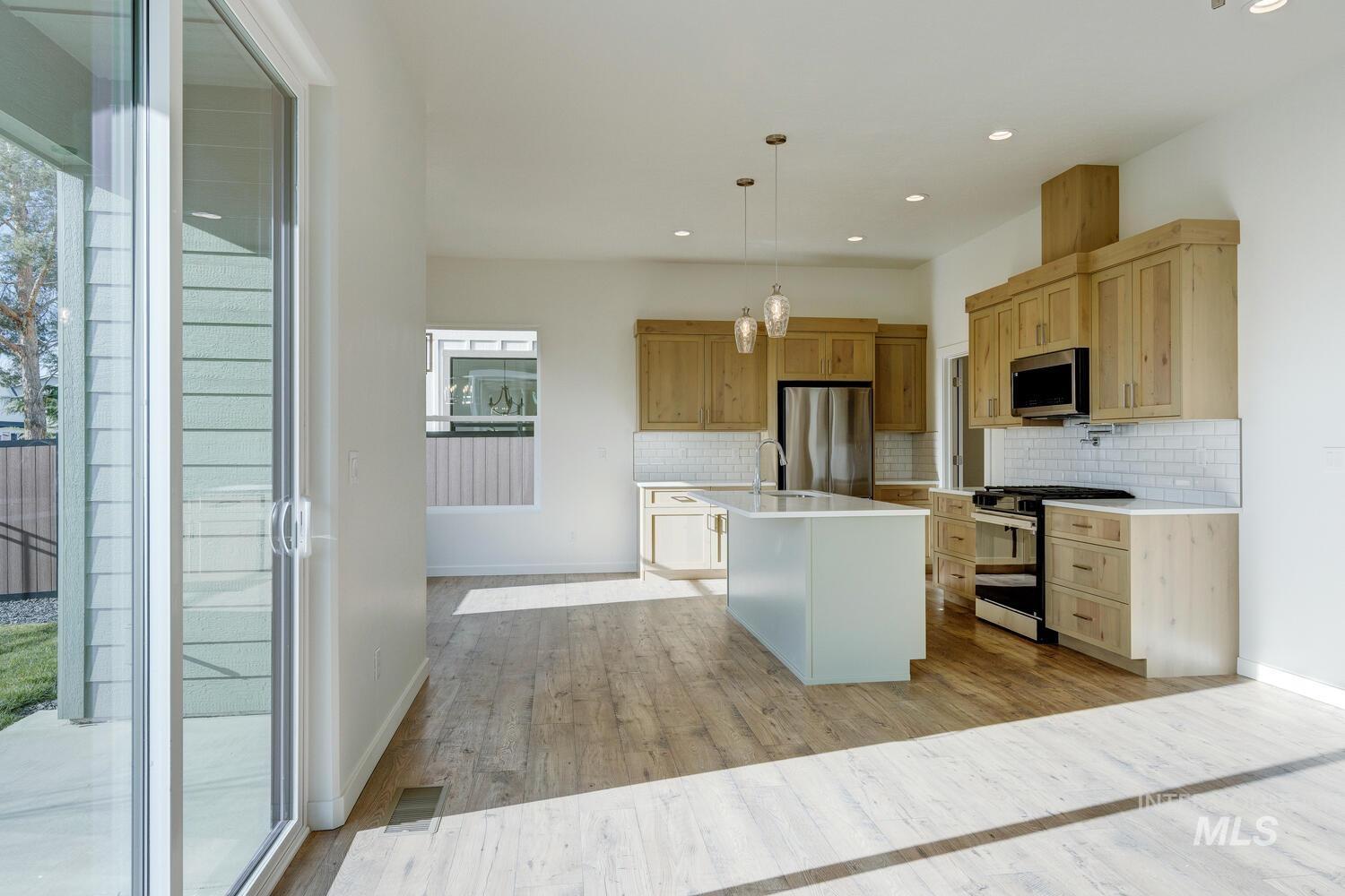 Kitchen featuring stainless steel appliances, hanging light fixtures, light wood-style floors, an island with sink, and tasteful backsplash