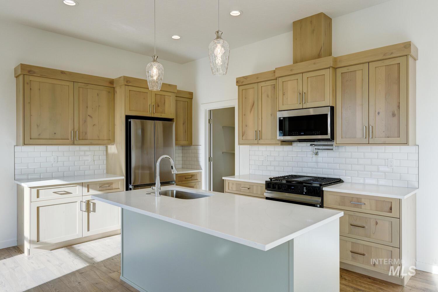 Kitchen featuring appliances with stainless steel finishes, decorative backsplash, hanging light fixtures, light brown cabinets, and recessed lighting