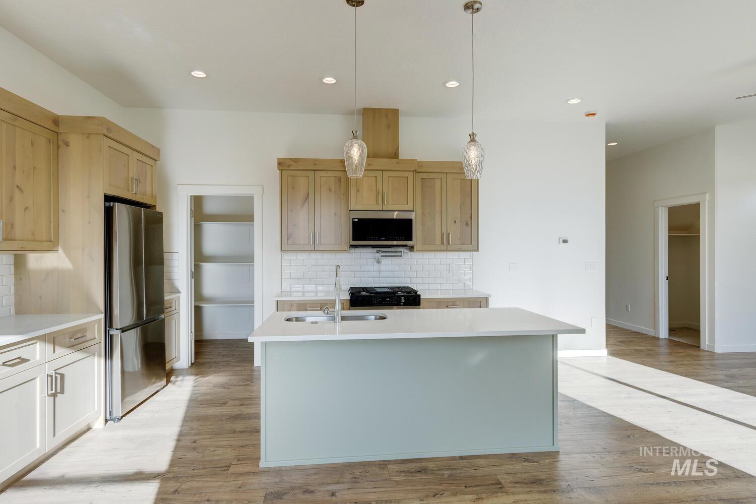 Kitchen with stainless steel appliances, a center island with sink, tasteful backsplash, light wood-style flooring, and decorative light fixtures