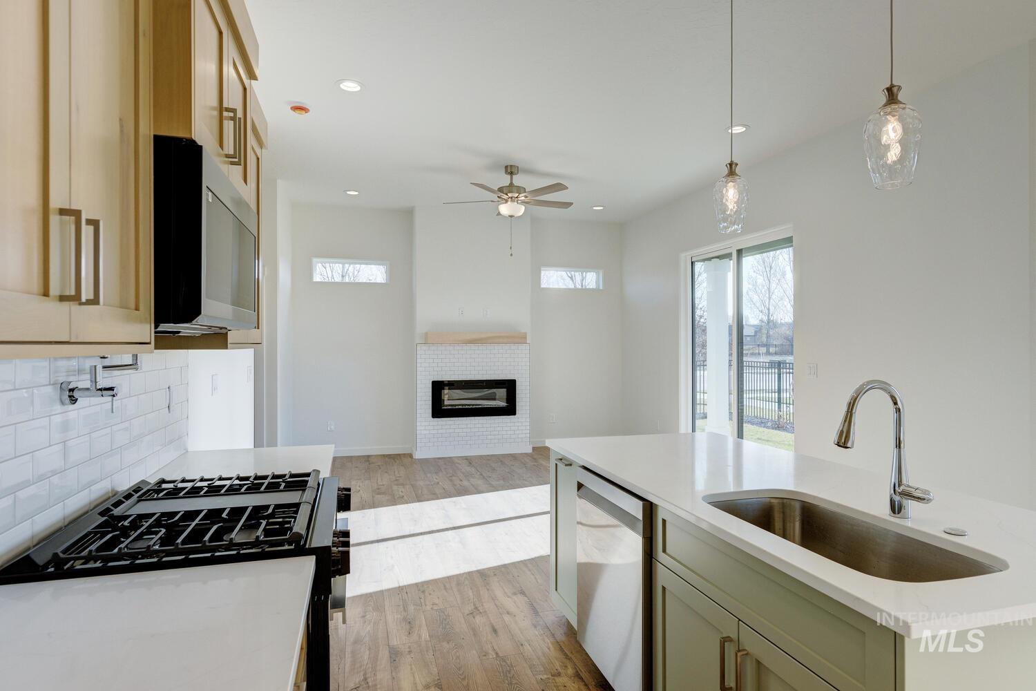 Kitchen featuring decorative light fixtures, light stone countertops, range with gas stovetop, ceiling fan, and light wood-type flooring