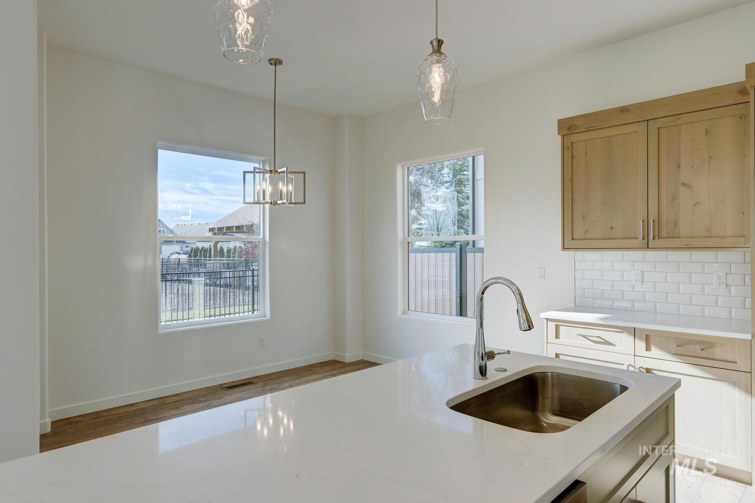 Kitchen featuring backsplash, light stone counters, pendant lighting, light wood finished floors, and a chandelier
