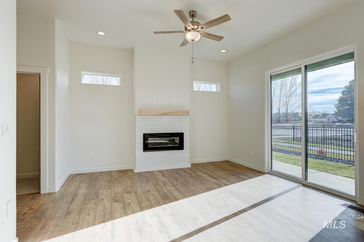 Unfurnished living room with light wood-type flooring, healthy amount of natural light, a tiled fireplace, ceiling fan, and recessed lighting