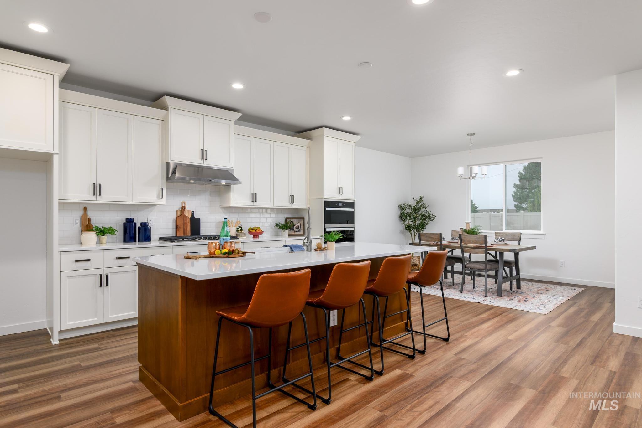 Kitchen with a center island with sink, decorative backsplash, a breakfast bar, recessed lighting, and white cabinetry