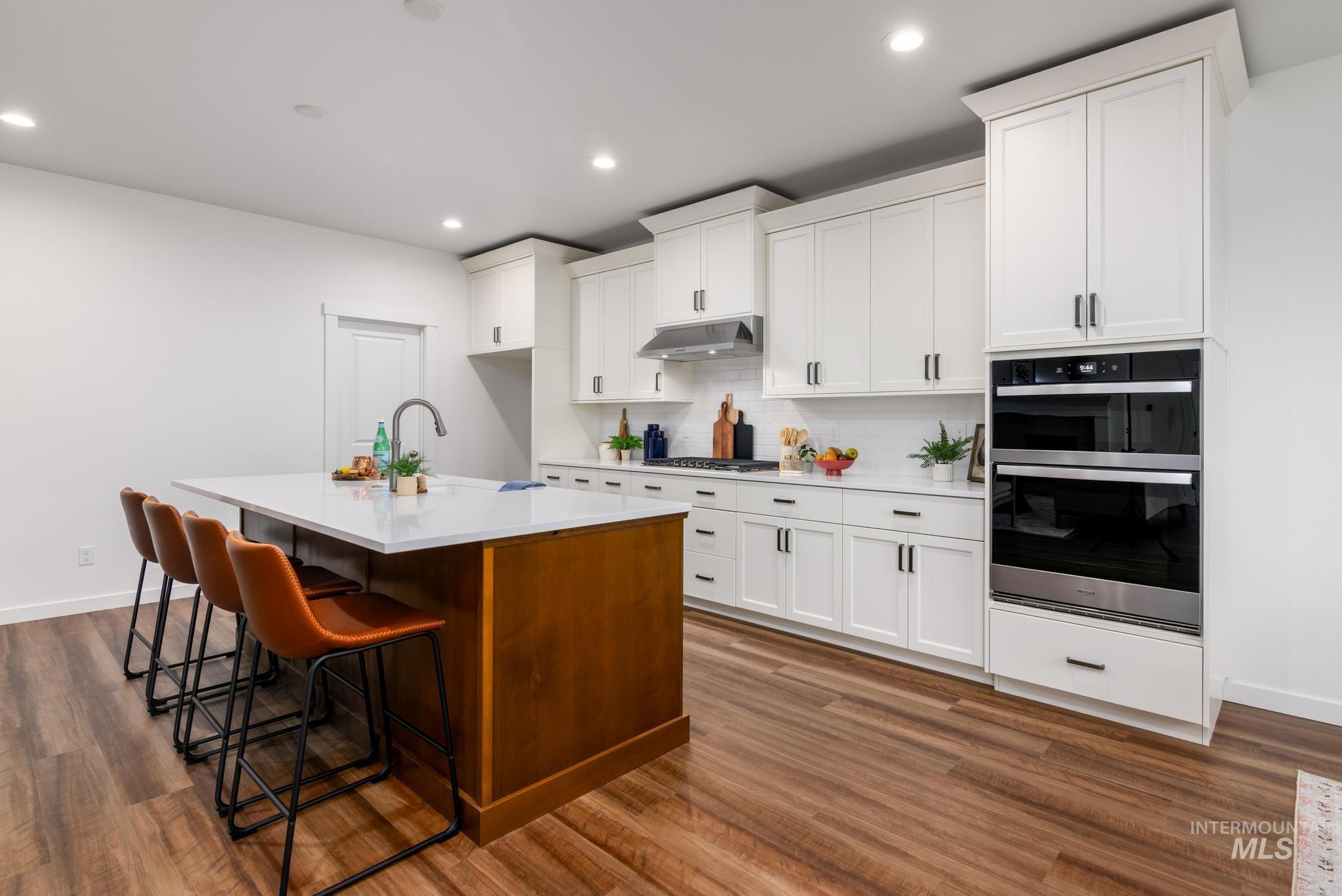 Kitchen with backsplash, dark wood-style flooring, a breakfast bar area, white cabinetry, and an island with sink