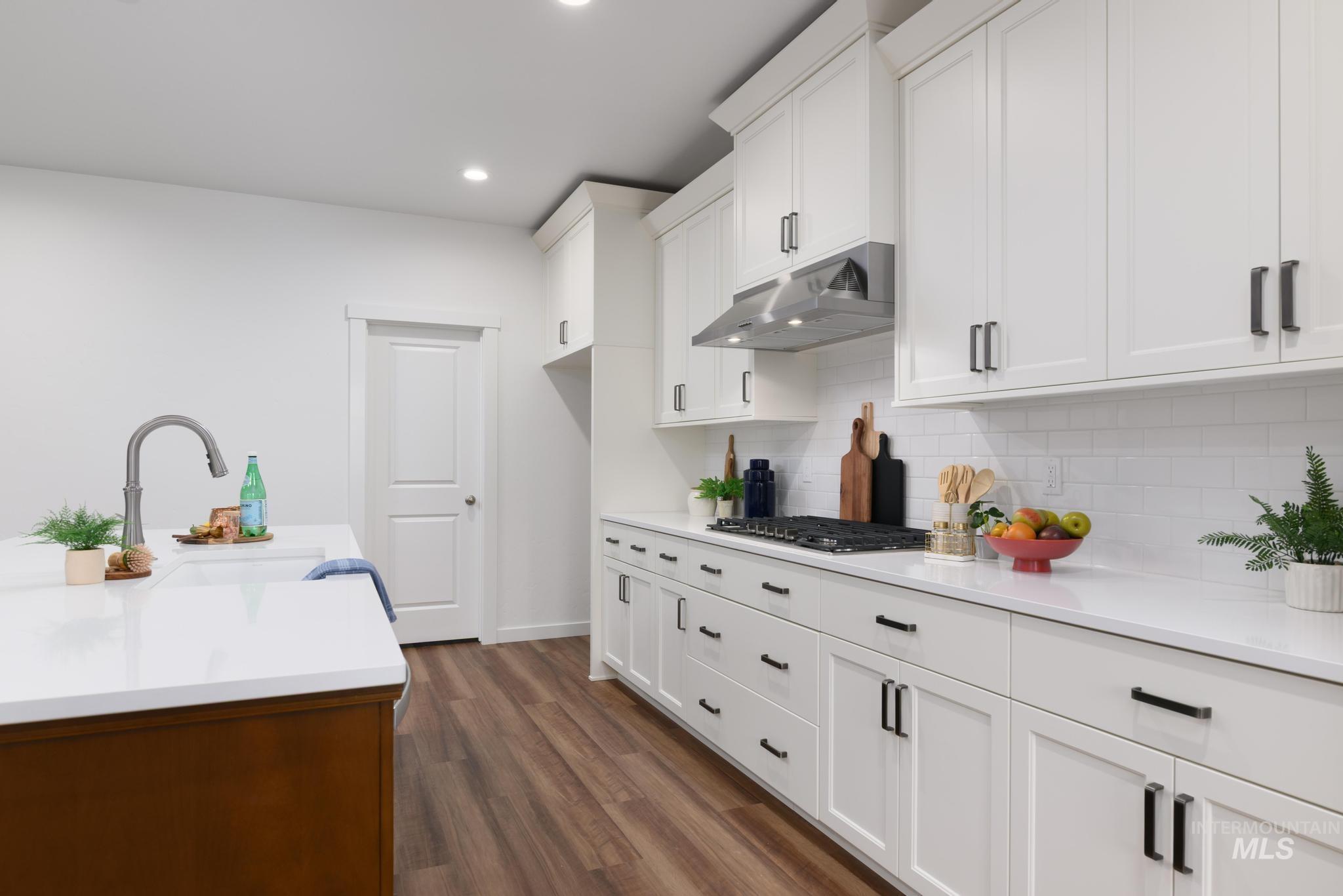 Kitchen featuring dark wood-style flooring, white cabinets, under cabinet range hood, backsplash, and light stone counters