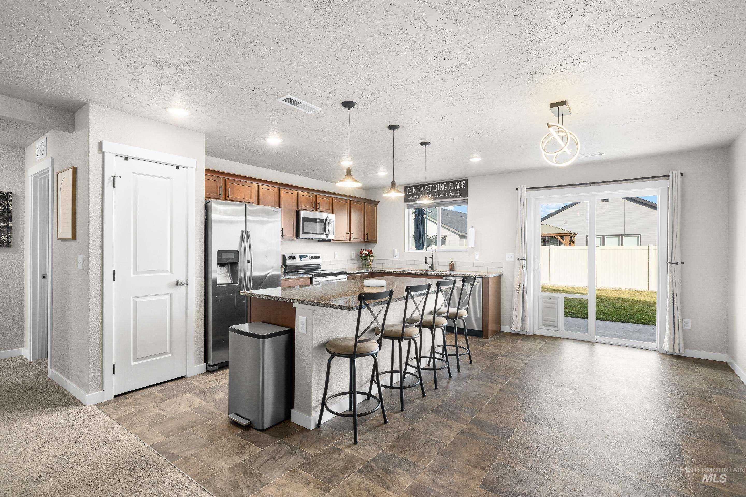 Kitchen featuring a kitchen breakfast bar, stainless steel appliances, hanging light fixtures, a kitchen island, and brown cabinetry