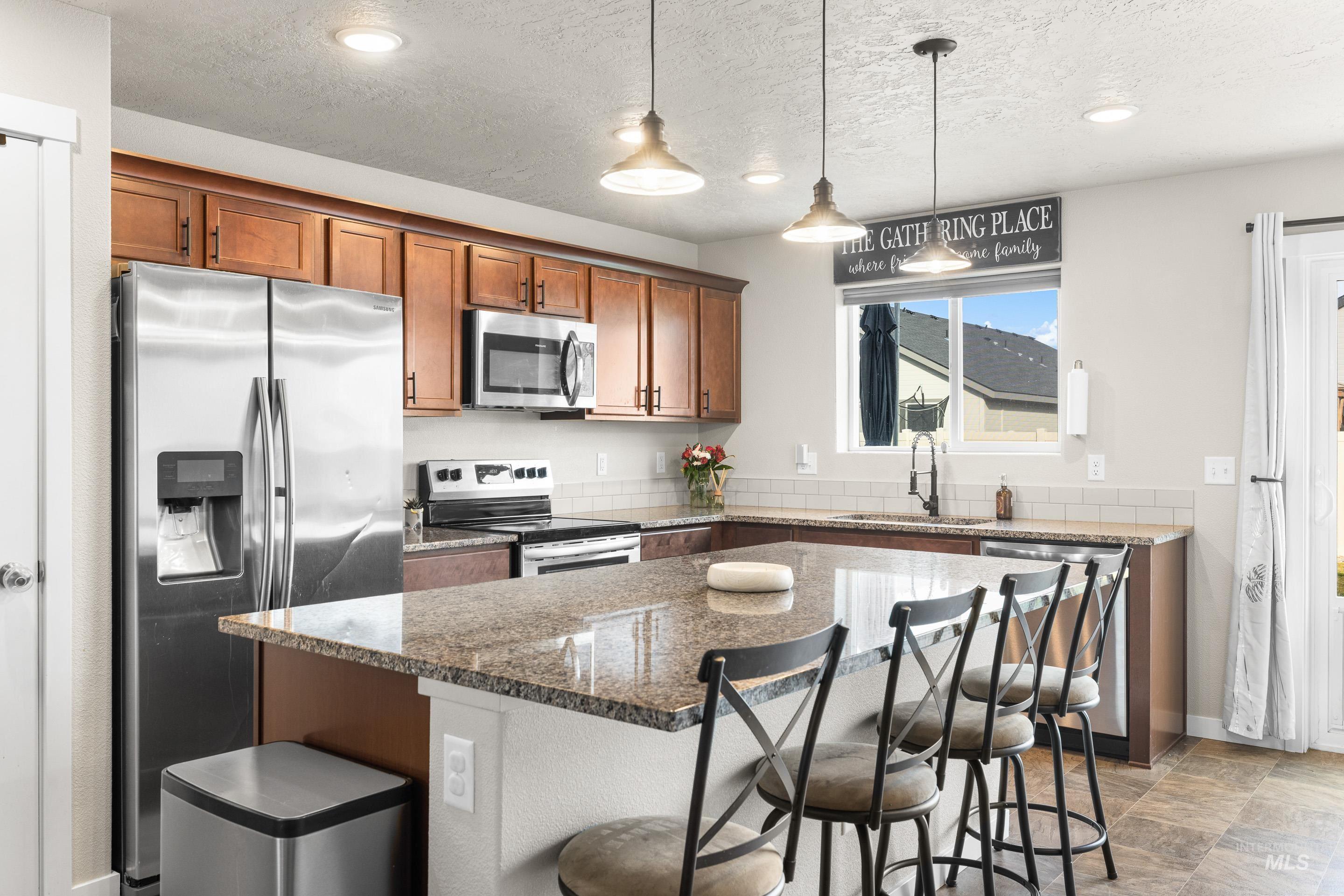 Kitchen with stainless steel appliances, dark stone counters, a kitchen bar, a center island, and brown cabinetry