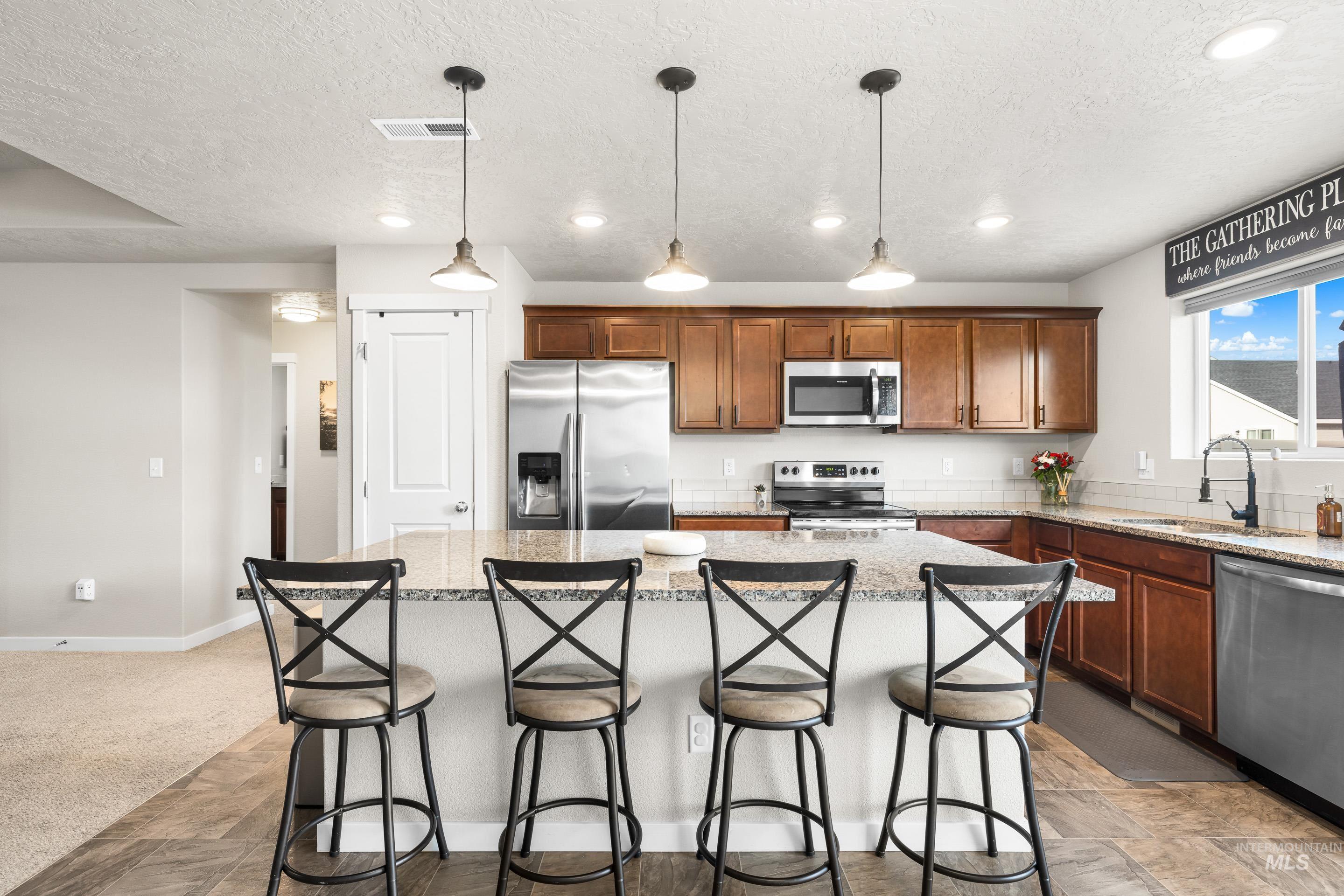 Kitchen with stainless steel appliances, brown cabinets, hanging light fixtures, a center island, and a breakfast bar