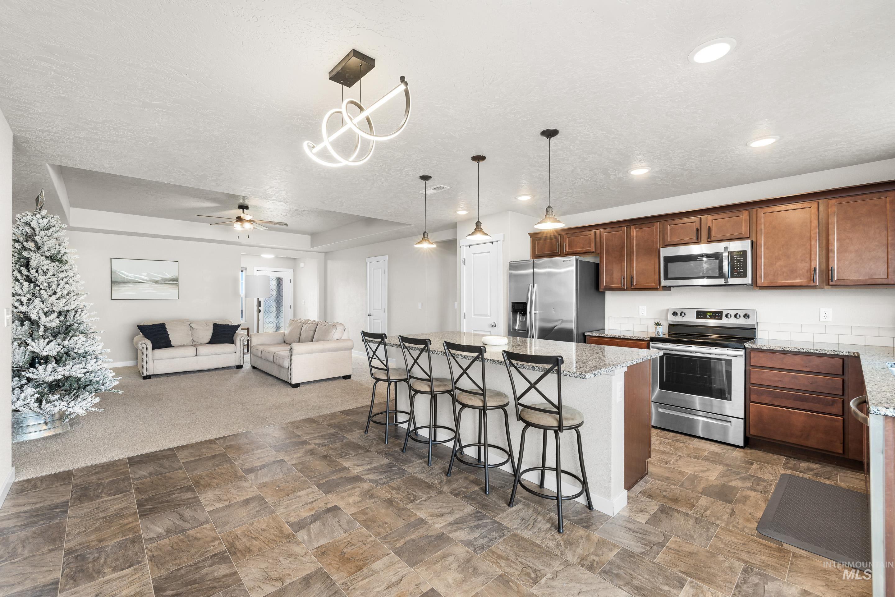 Kitchen featuring stainless steel appliances, a kitchen breakfast bar, open floor plan, light stone countertops, and dark carpet