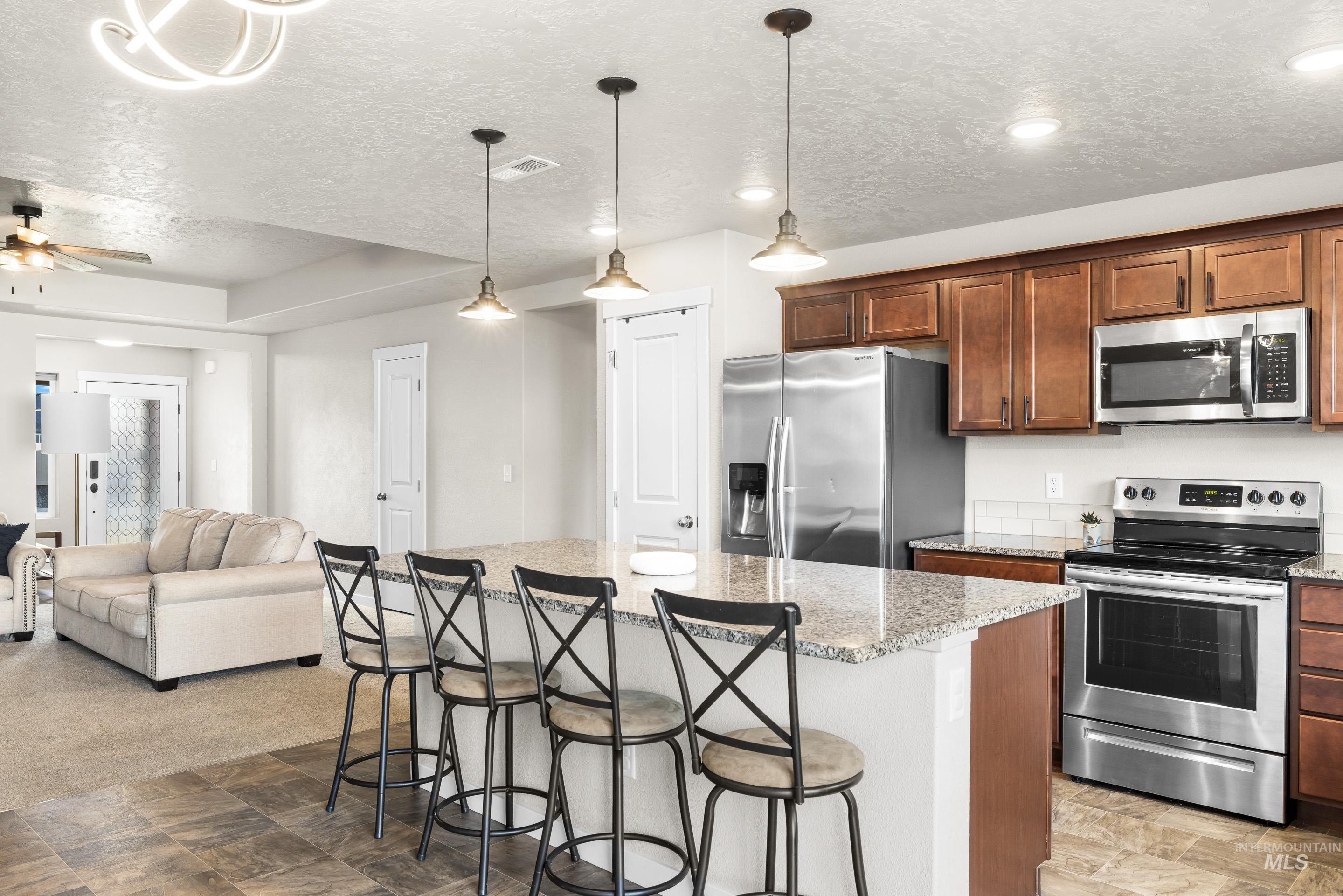 Kitchen with appliances with stainless steel finishes, a textured ceiling, a kitchen breakfast bar, pendant lighting, and a center island