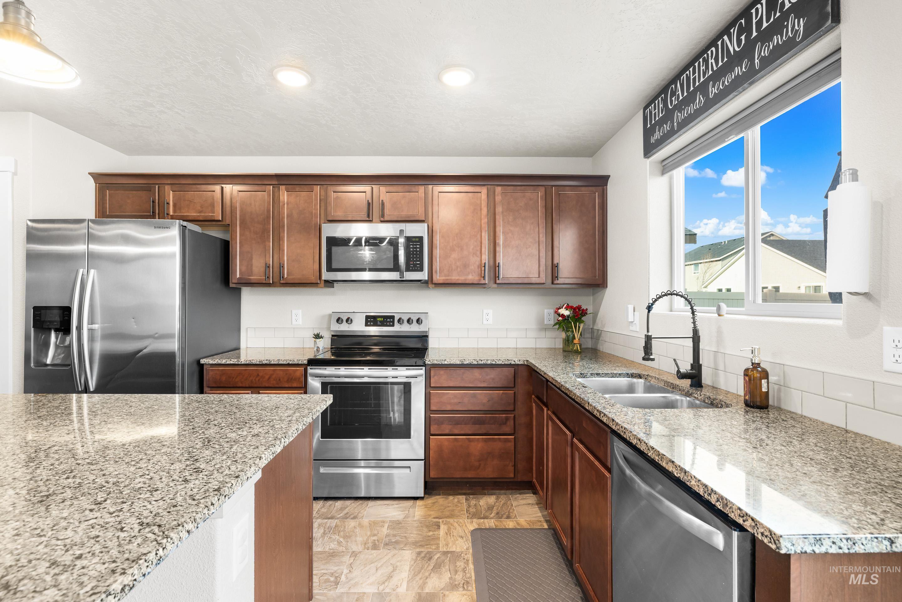 Kitchen featuring appliances with stainless steel finishes, light stone counters, recessed lighting, stone finish floors, and brown cabinetry