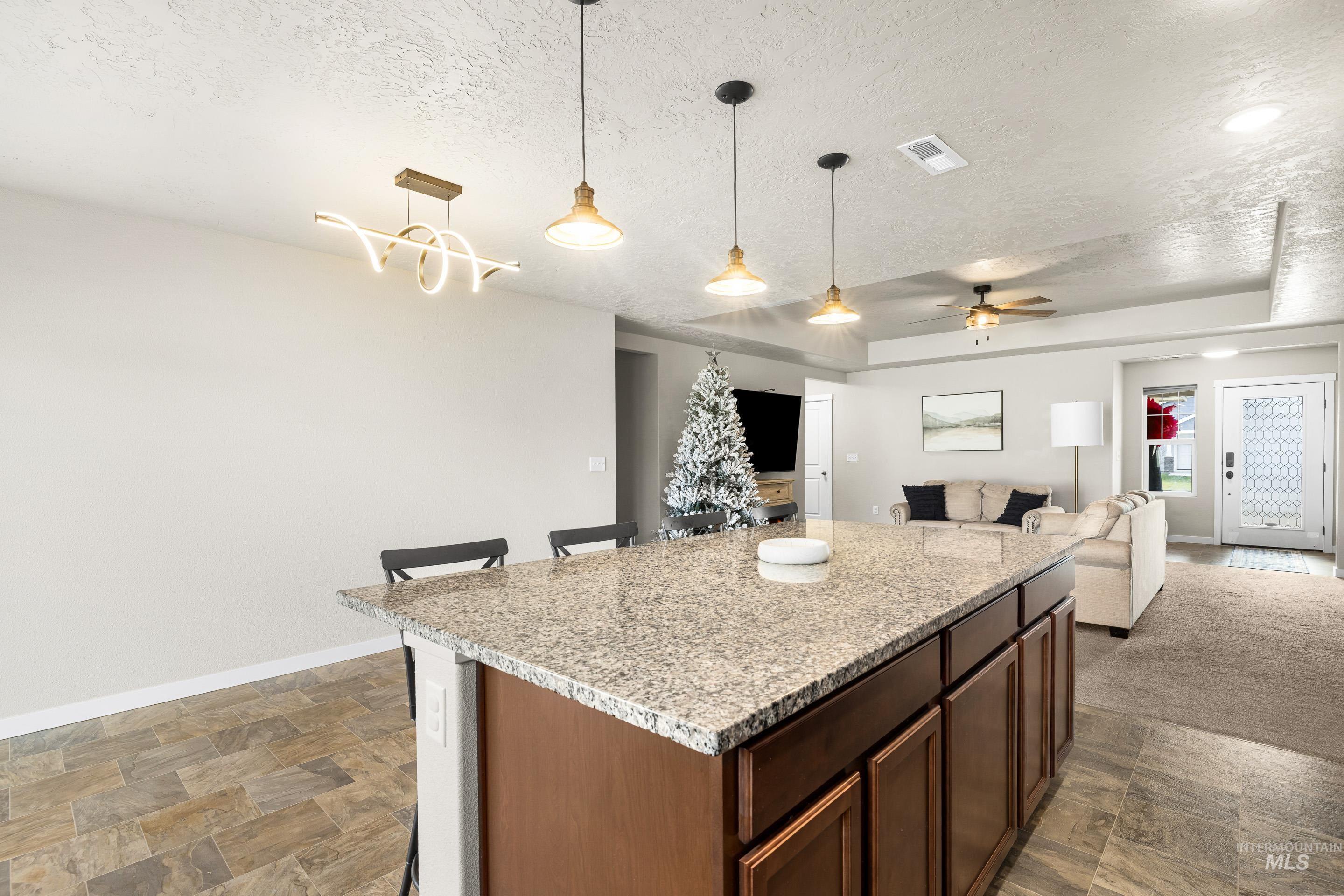 Kitchen with light stone countertops, hanging light fixtures, dark brown cabinetry, a textured ceiling, and a ceiling fan