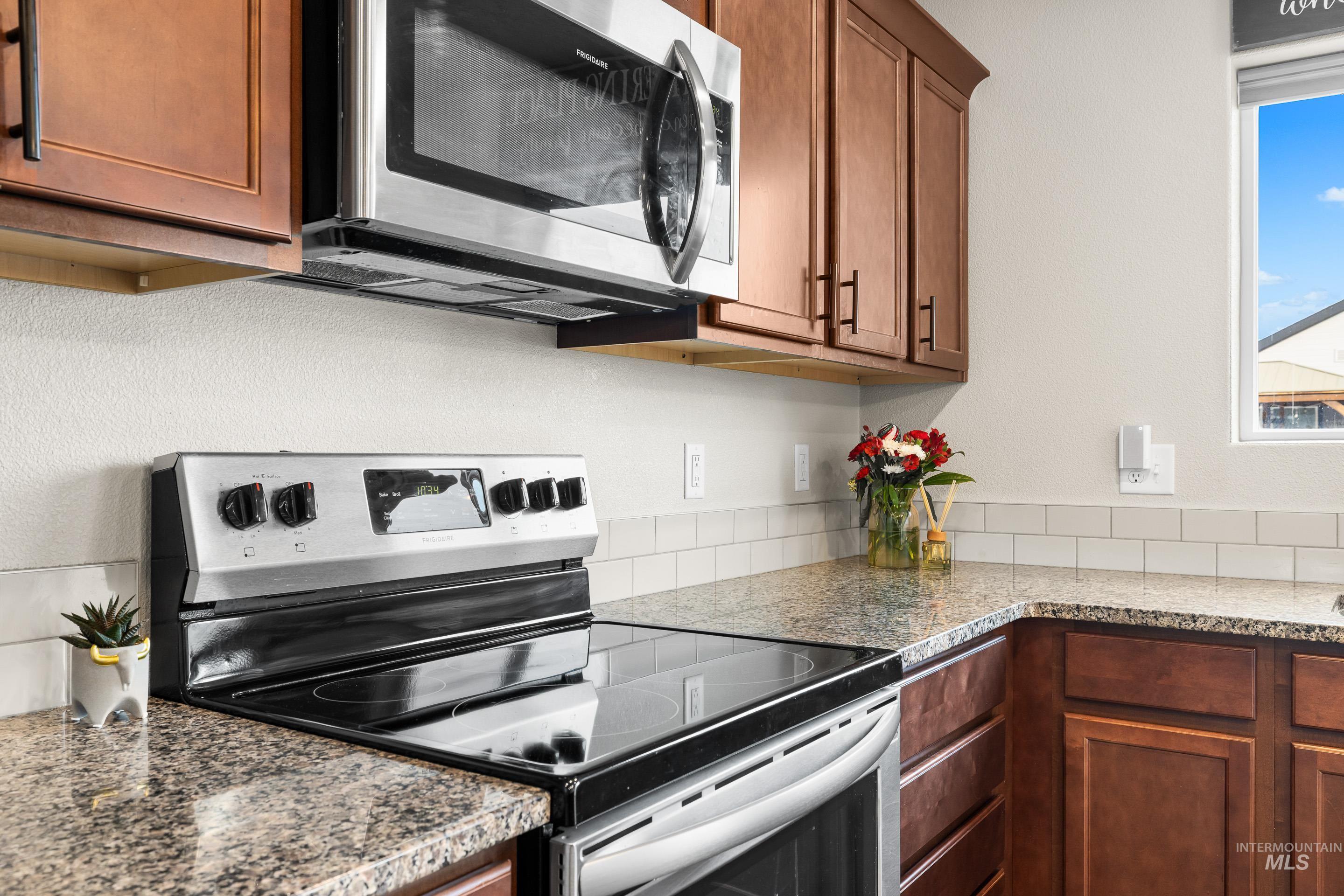 Kitchen featuring appliances with stainless steel finishes, brown cabinetry, and light stone counters