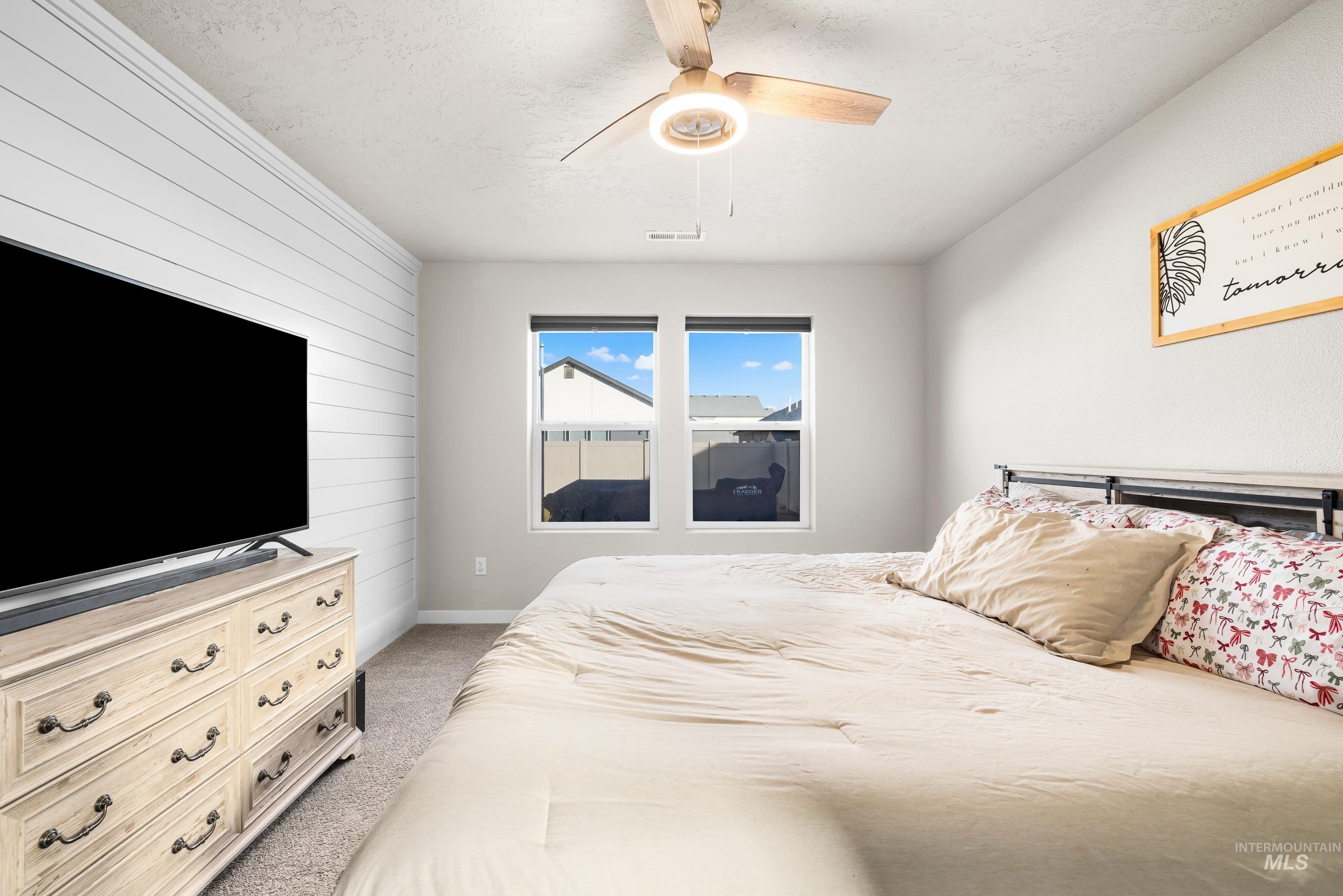 Bedroom featuring wooden walls, light colored carpet, a ceiling fan, and a textured ceiling