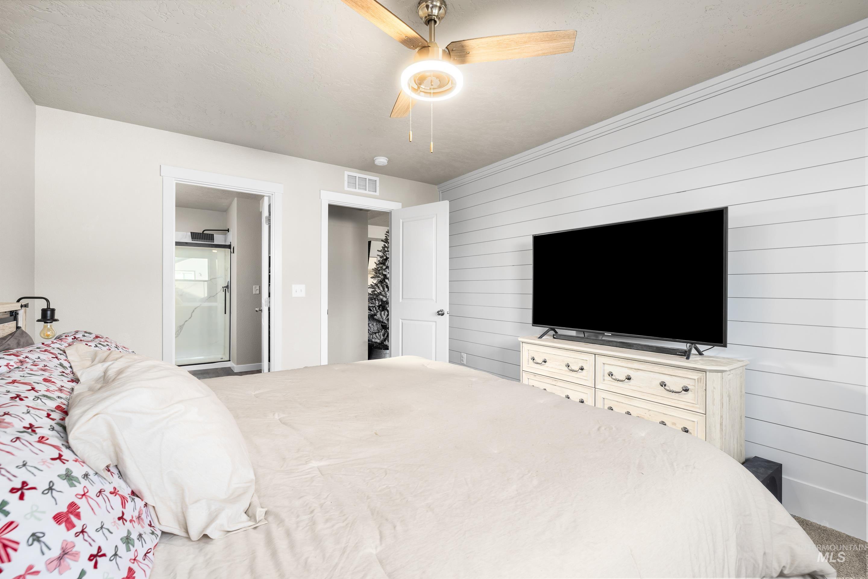 Bedroom with wooden walls, a ceiling fan, an accent wall, and ensuite bathroom