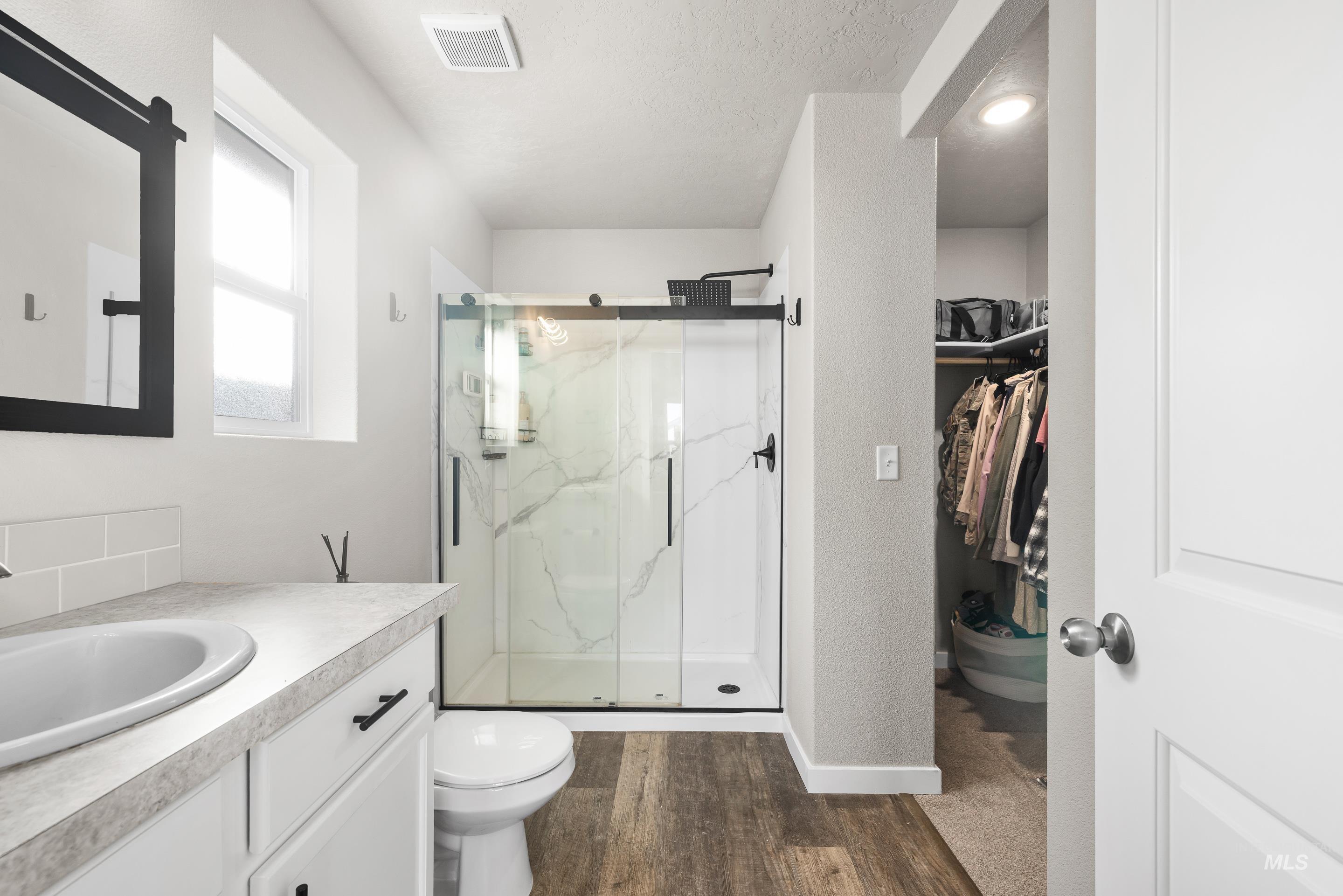 Full bathroom featuring vanity, a marble finish shower, a spacious closet, dark wood finished floors, and a textured ceiling