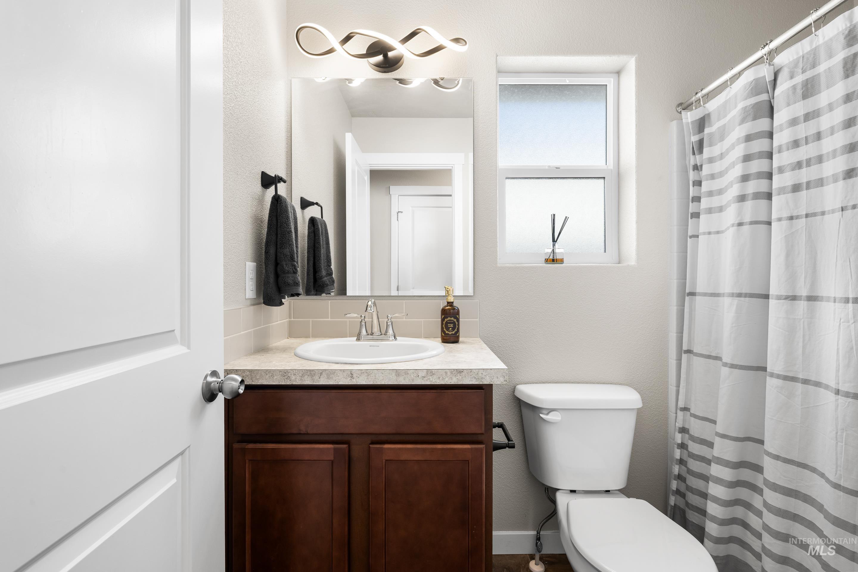 Bathroom with curtained shower, vanity, a textured wall, and decorative backsplash